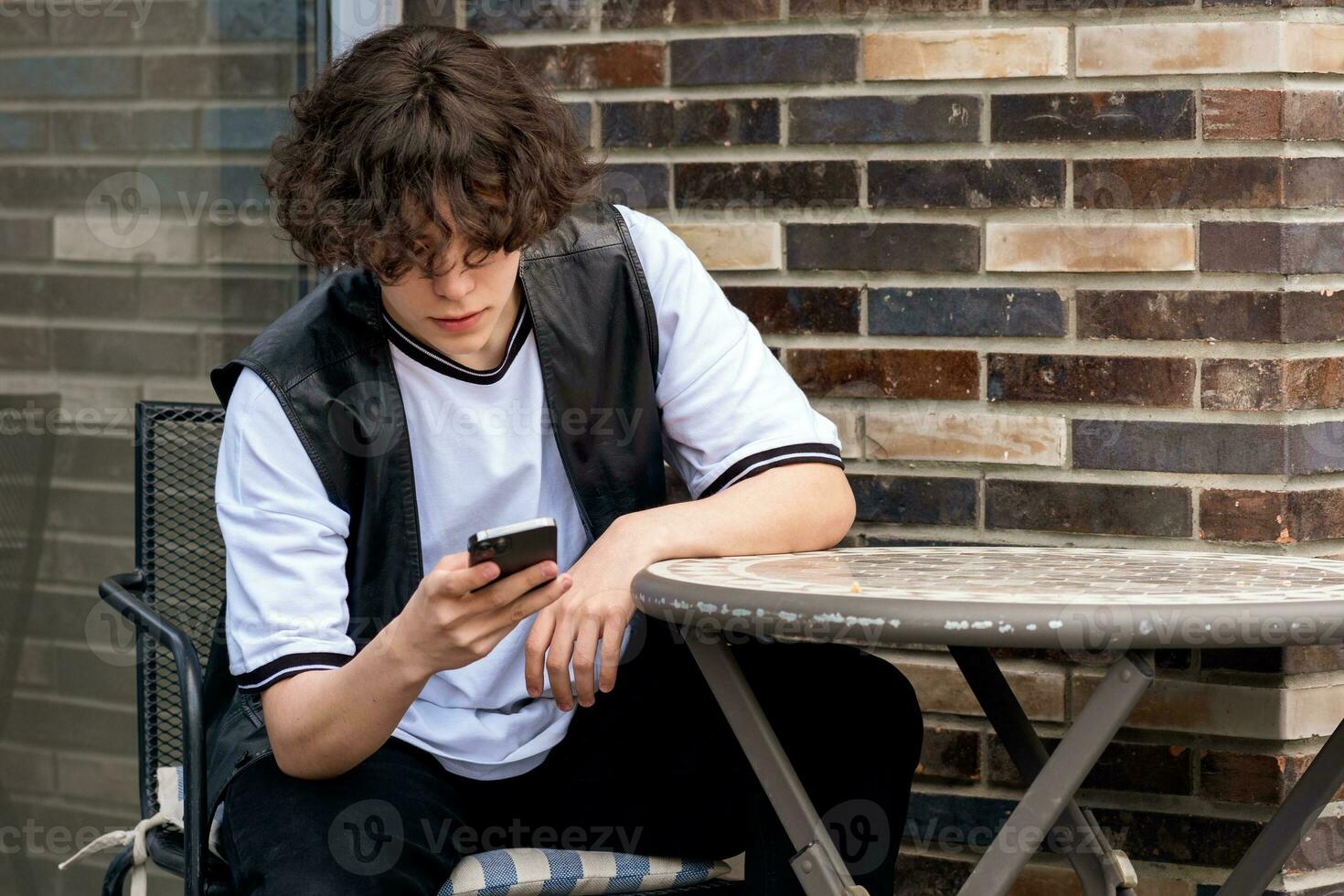 young man typing something on the phone while sitting at an outdoor cafeteria table photo