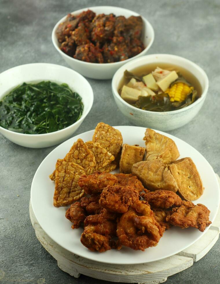 tempe and crispy chicken and tamarind vegetables and spinach, on a wooden table, selective focus photo