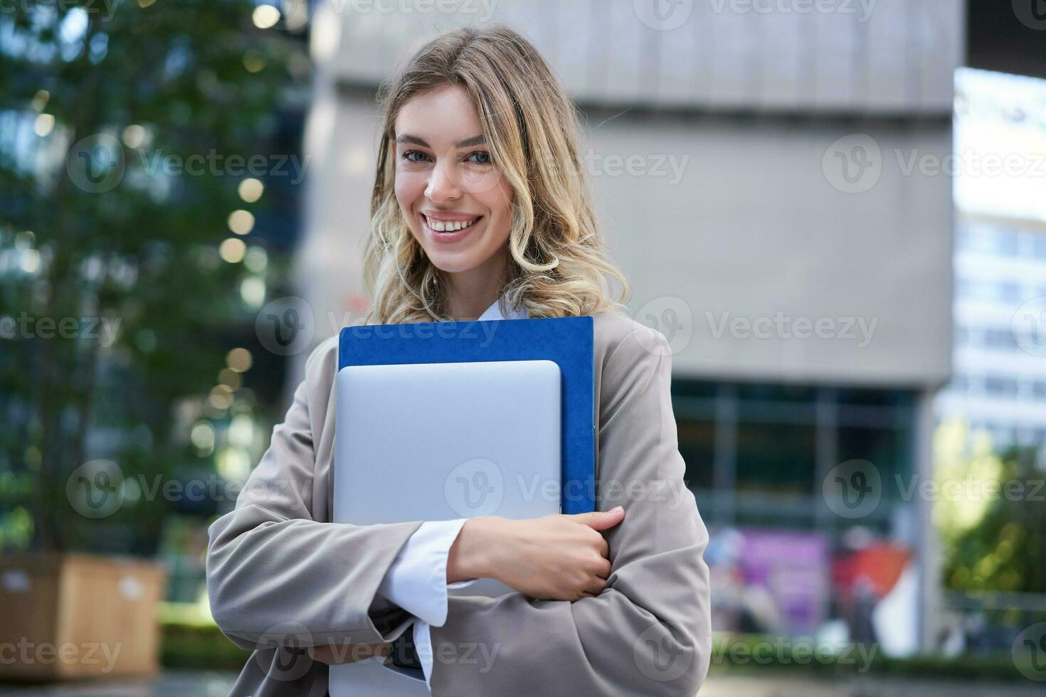 retrato de joven corporativo mujer, oficina gerente caminando en calle con ordenador portátil y trabajo carpeta, sonriente foto