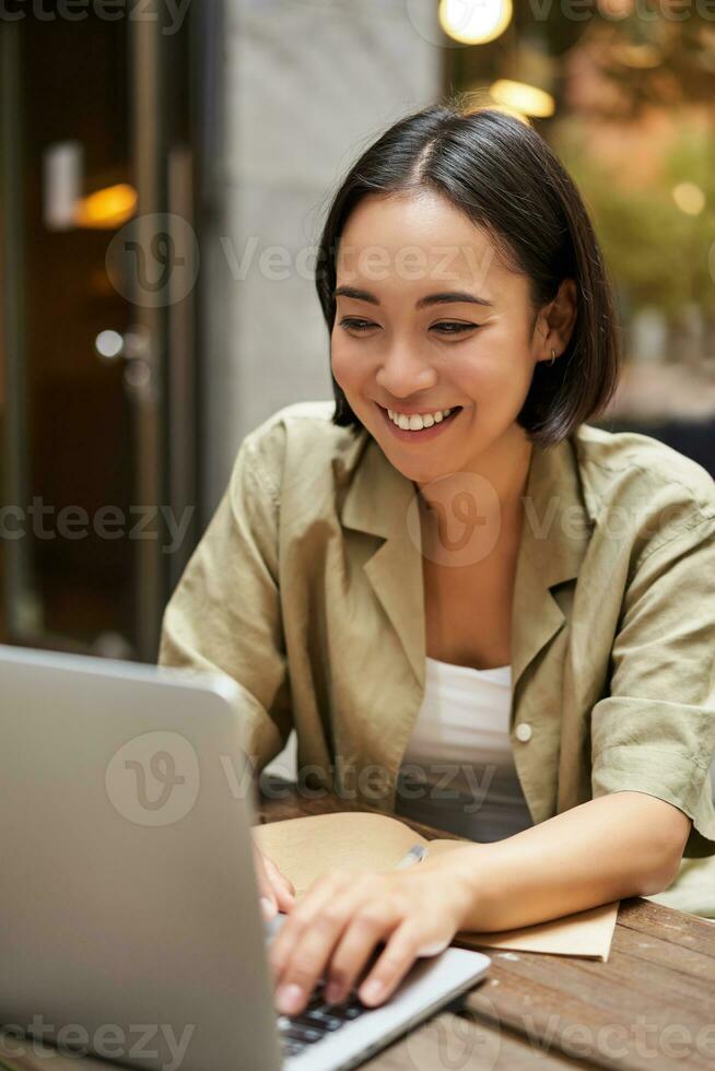 Smiling young woman working from cafe or co-working space, sitting with laptop, studying or doing homework, looking happy photo