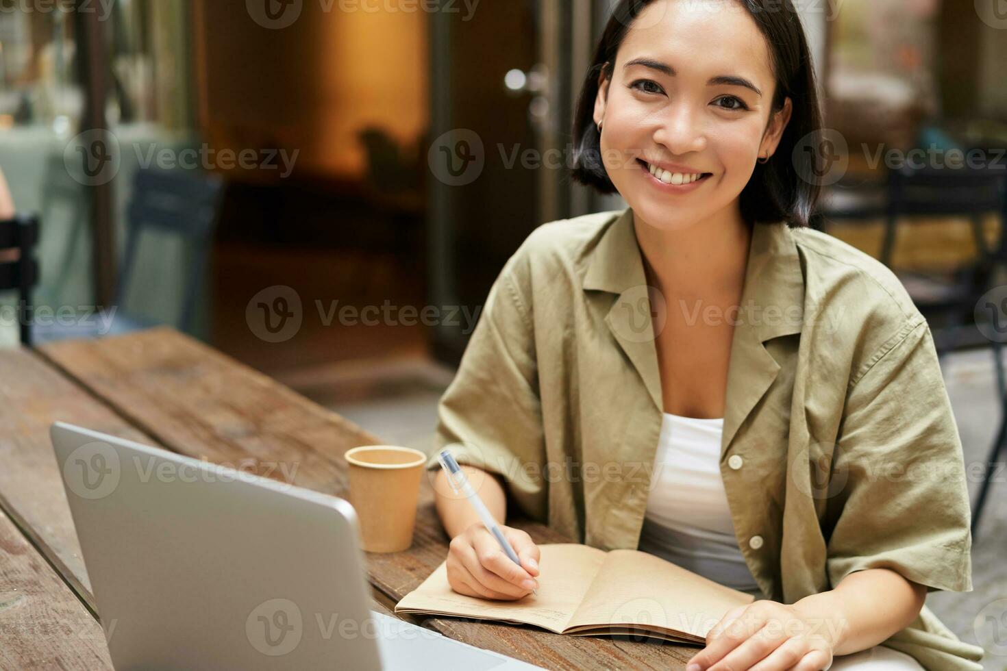 Portrait of young korean girl making notes, listening online meeting, lecture, looking at laptop screen, working remotely from cafe photo