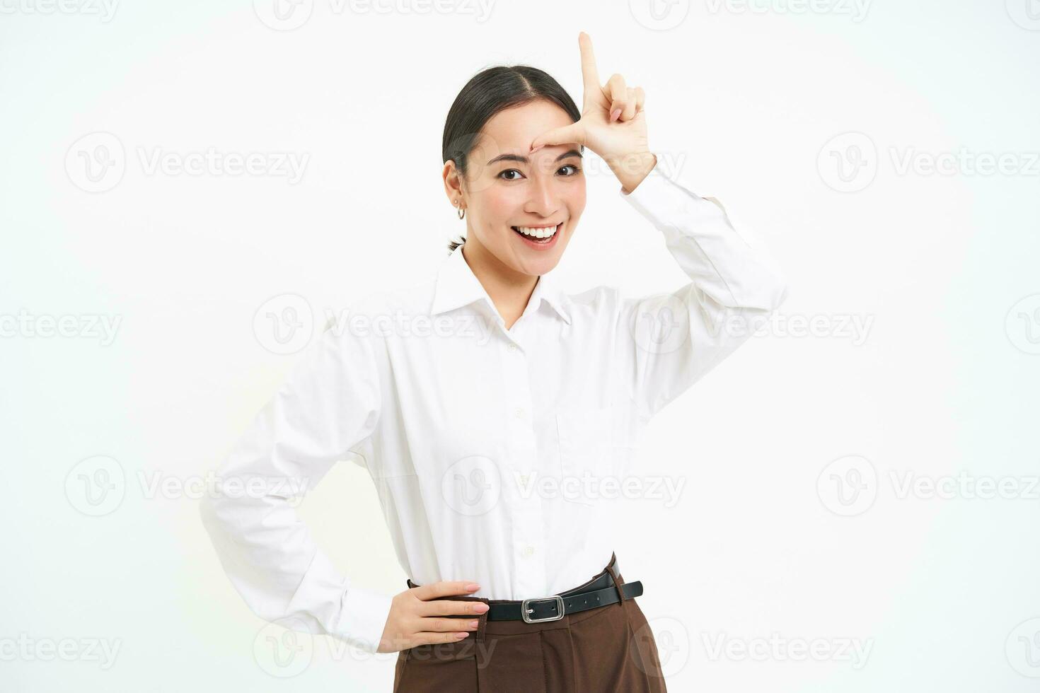 Successful businesswoman looks confident, shows L letter, loser sign on forehaed, feels proud of herself, smiles pleased over white background photo