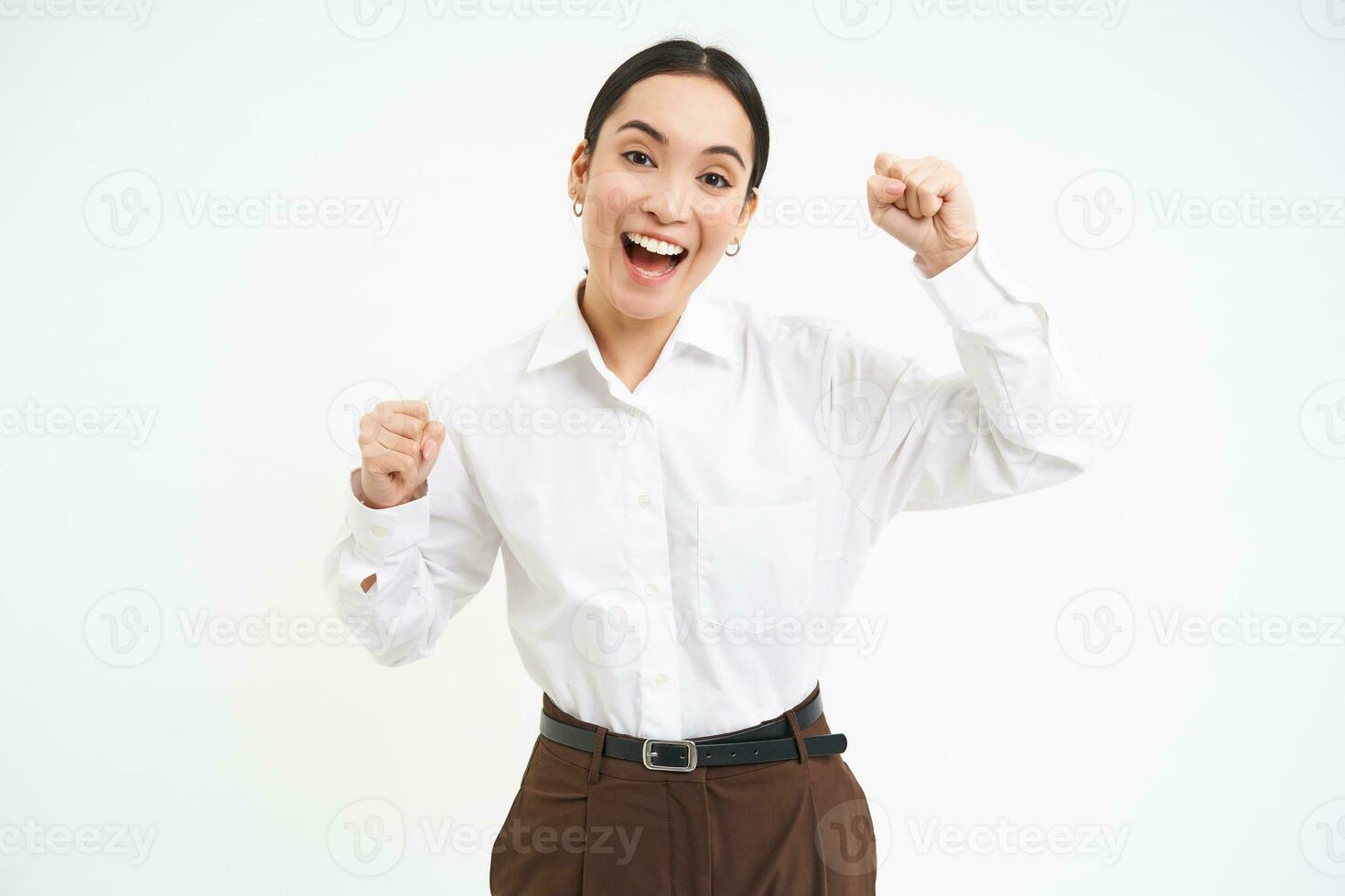 Enthusiastic businesswoman celebrates, raises hands and dances, winning, feels excited, triumphing, white background photo