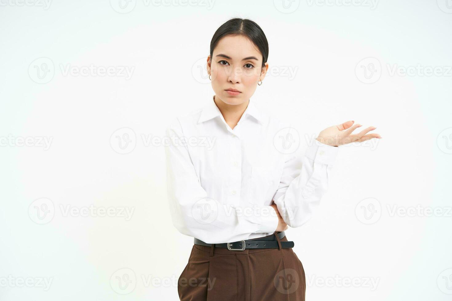 Professional businesswoman, looks puzzled at camera, extends one hand with confused face expression, white background photo