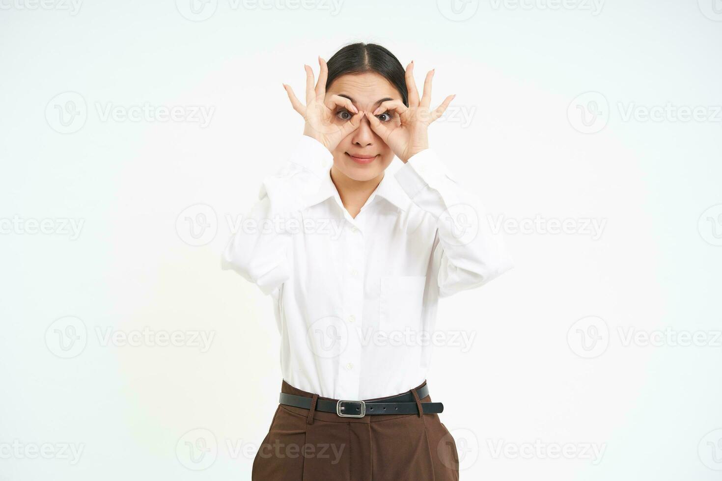 Funny korean woman makes hand glasses sign and looks through, stands over white background photo