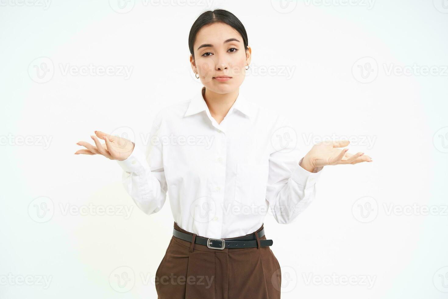 Clueless asian corporate woman, shrugs shoulders with puzzled face expression, stands confused, white background photo