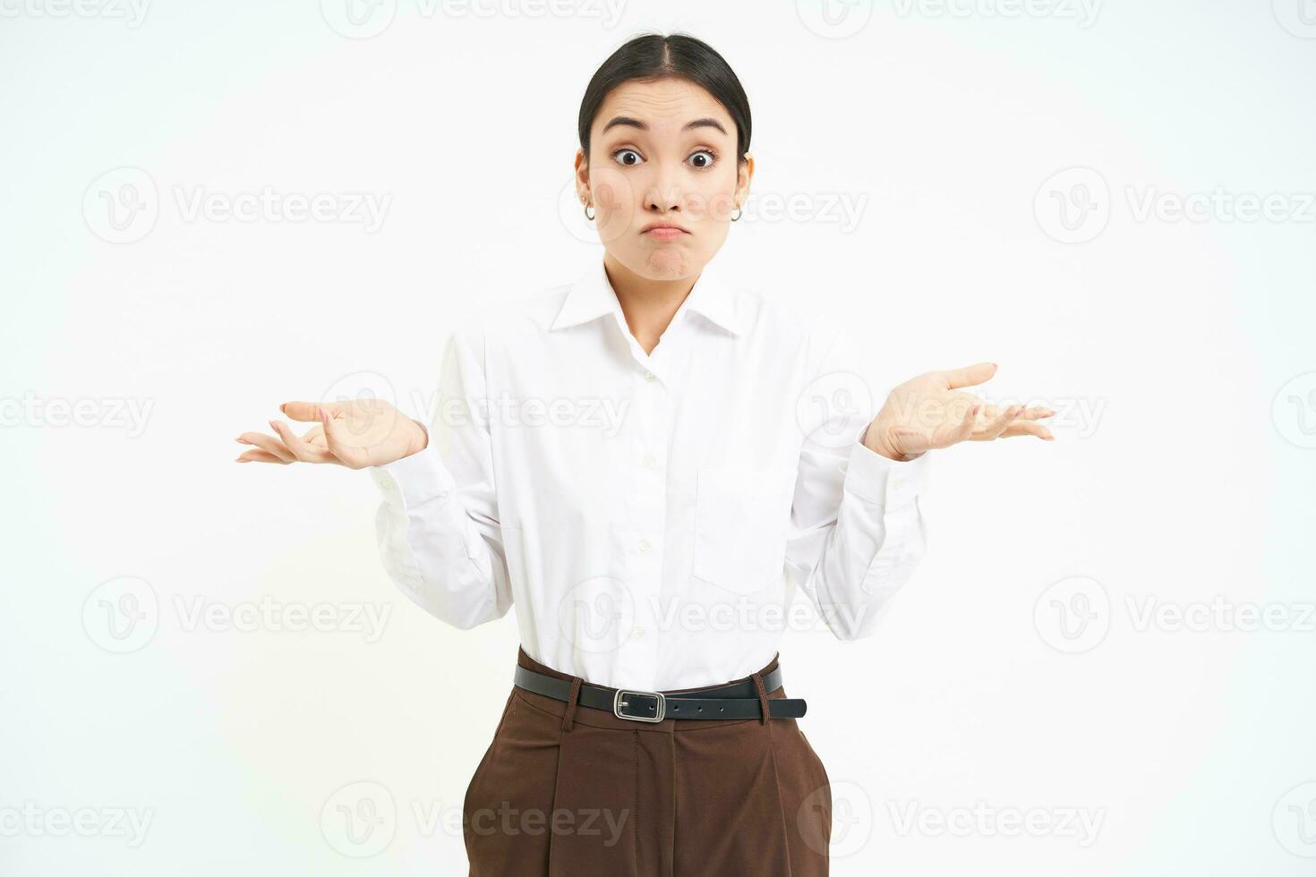 Clueless asian corporate woman, shrugs shoulders with puzzled face expression, stands confused, white background photo