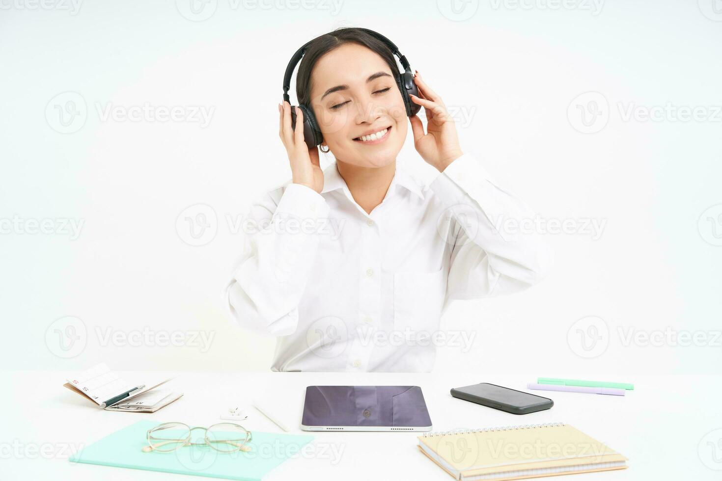 Smiling businesswoman in headphones, sits at office desk listens music and relaxes, rests after work, white background photo