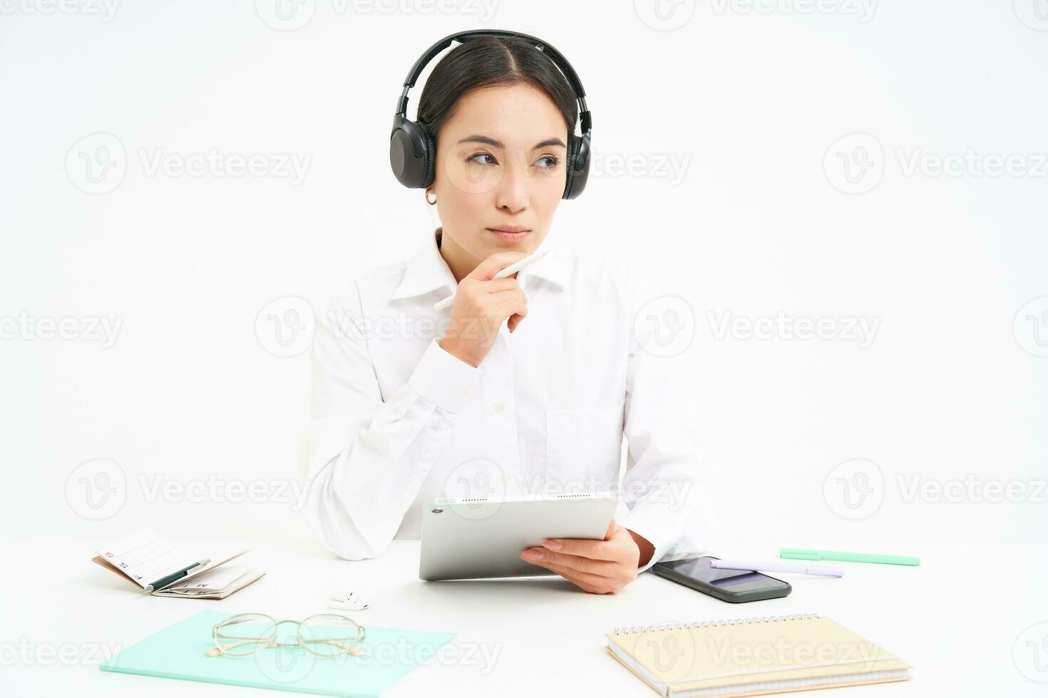 Portrait of cute office woman in headphones, sits at workplace, works with digital tablet, listens to online course, white background photo