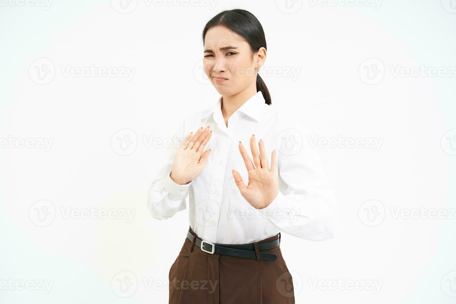 Stop, stay back. Young asian woman rejects smth, pulls away, holds hands extended to refuse, disapprove something, white background photo