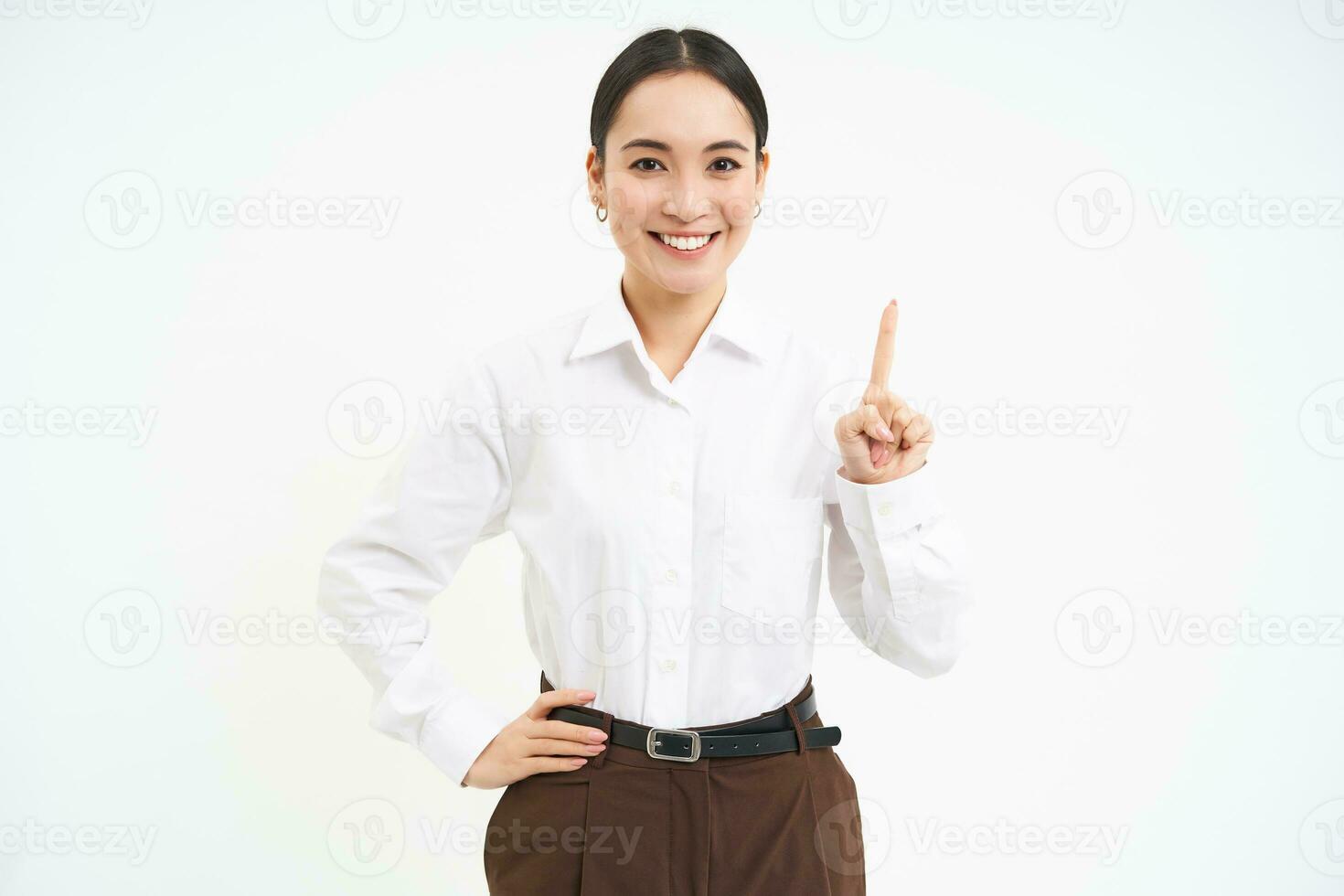 Confident young female manager, asian woman shows number one finger, explains smth, stands over white background photo