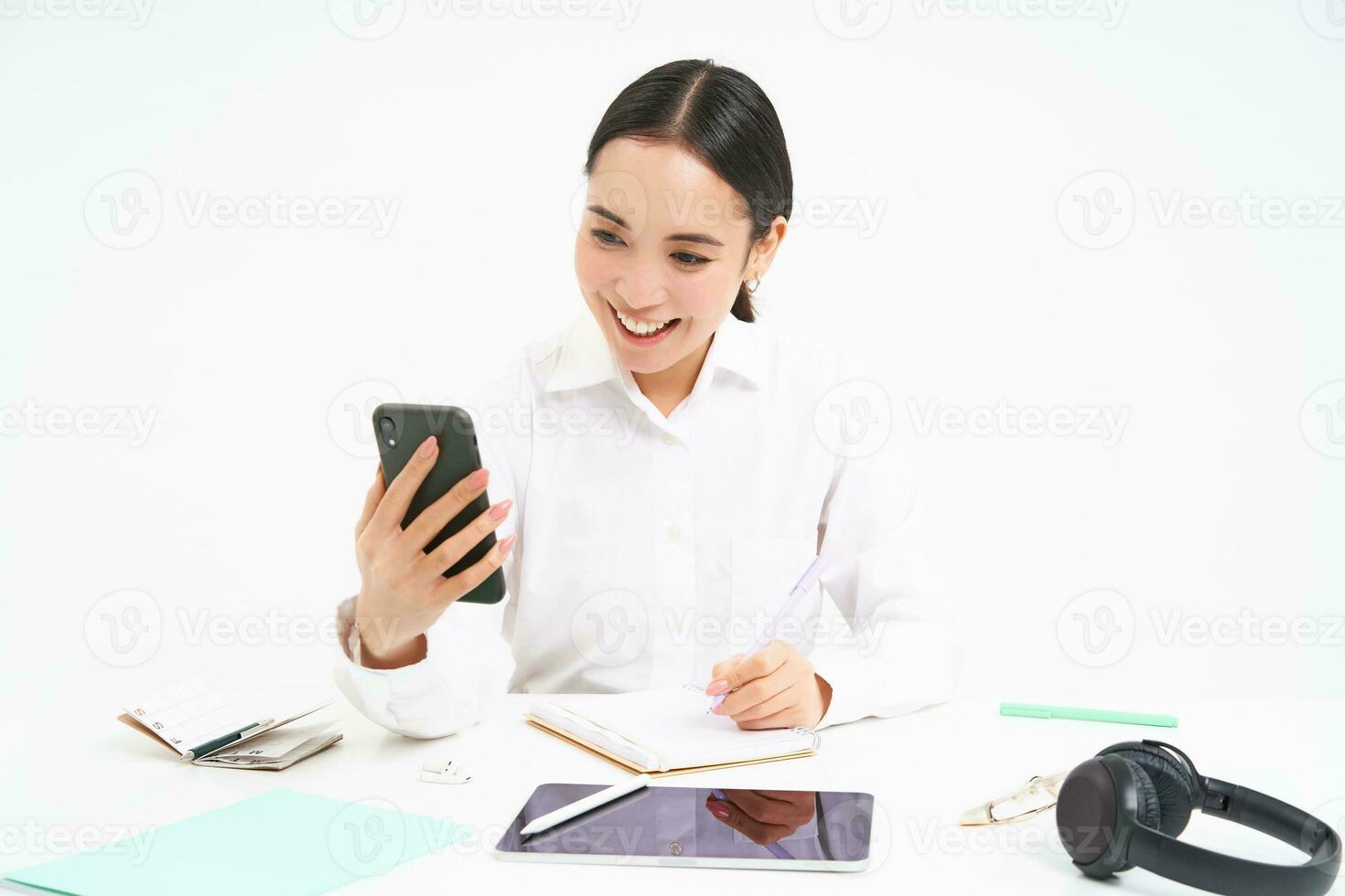 Young woman professional, businesswoman has a meeting on video chat, talks to mobile phone with client, stands over white background photo