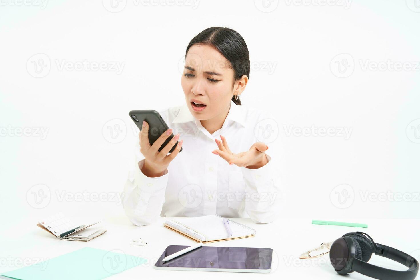 Angry lady boss, businesswoman looks frustrated, talks on mobile phone, has an argument during conversation on cellphone, sits in her office, white background photo