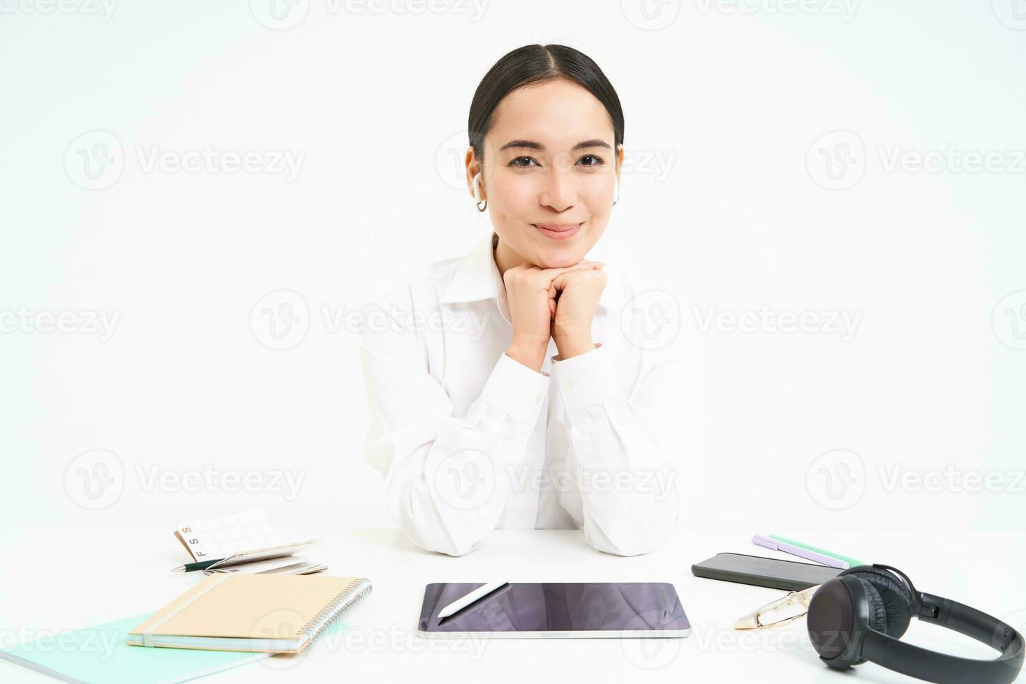 Office and profession. Portrait of successful businesswoman sits behind table with digital tablet, headphones, smartphone and documents, smiling at camera photo