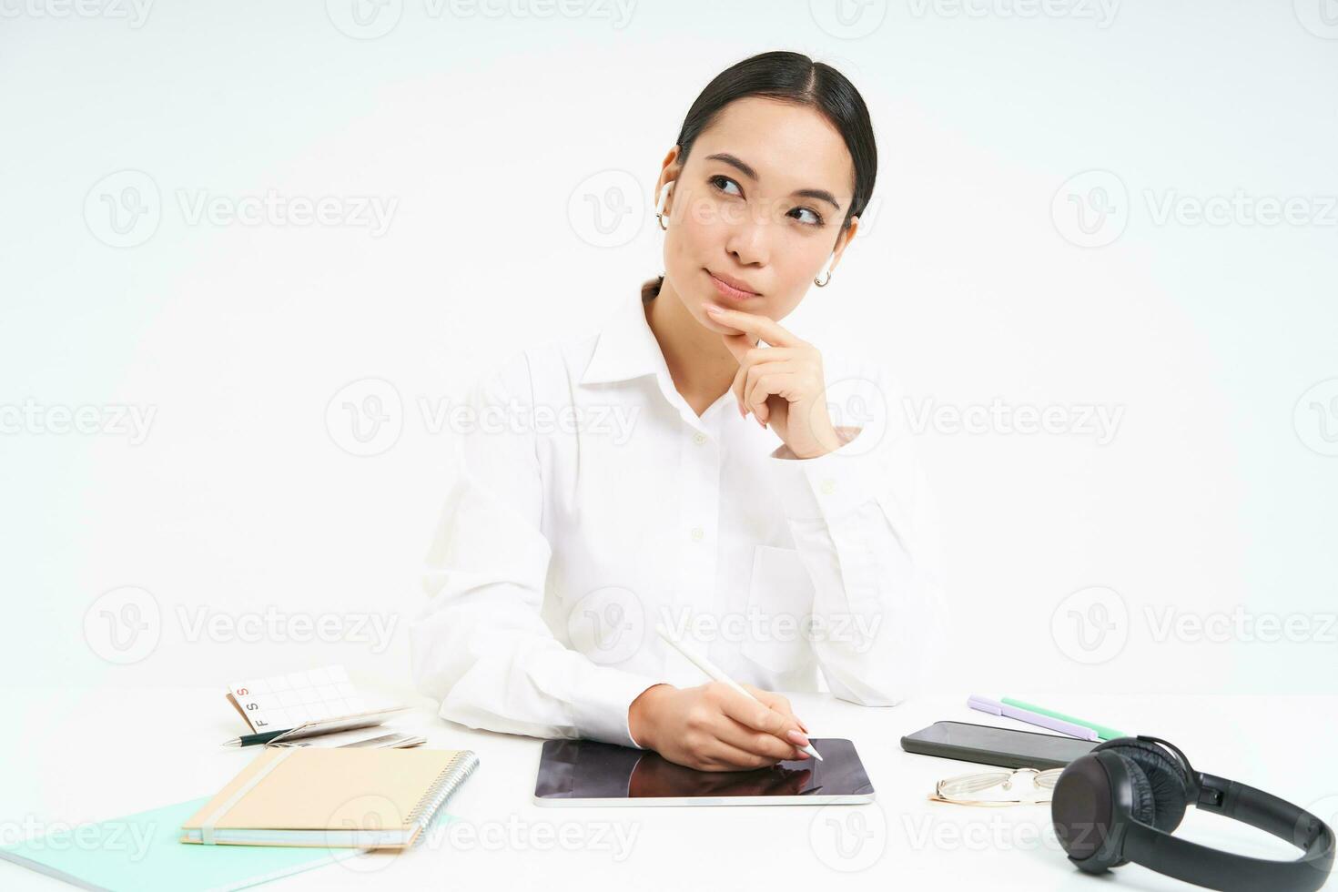 Image of korean businesswoman in earphones, listens music and works on digital tablet, holds pen, preparing project in her office, white background photo
