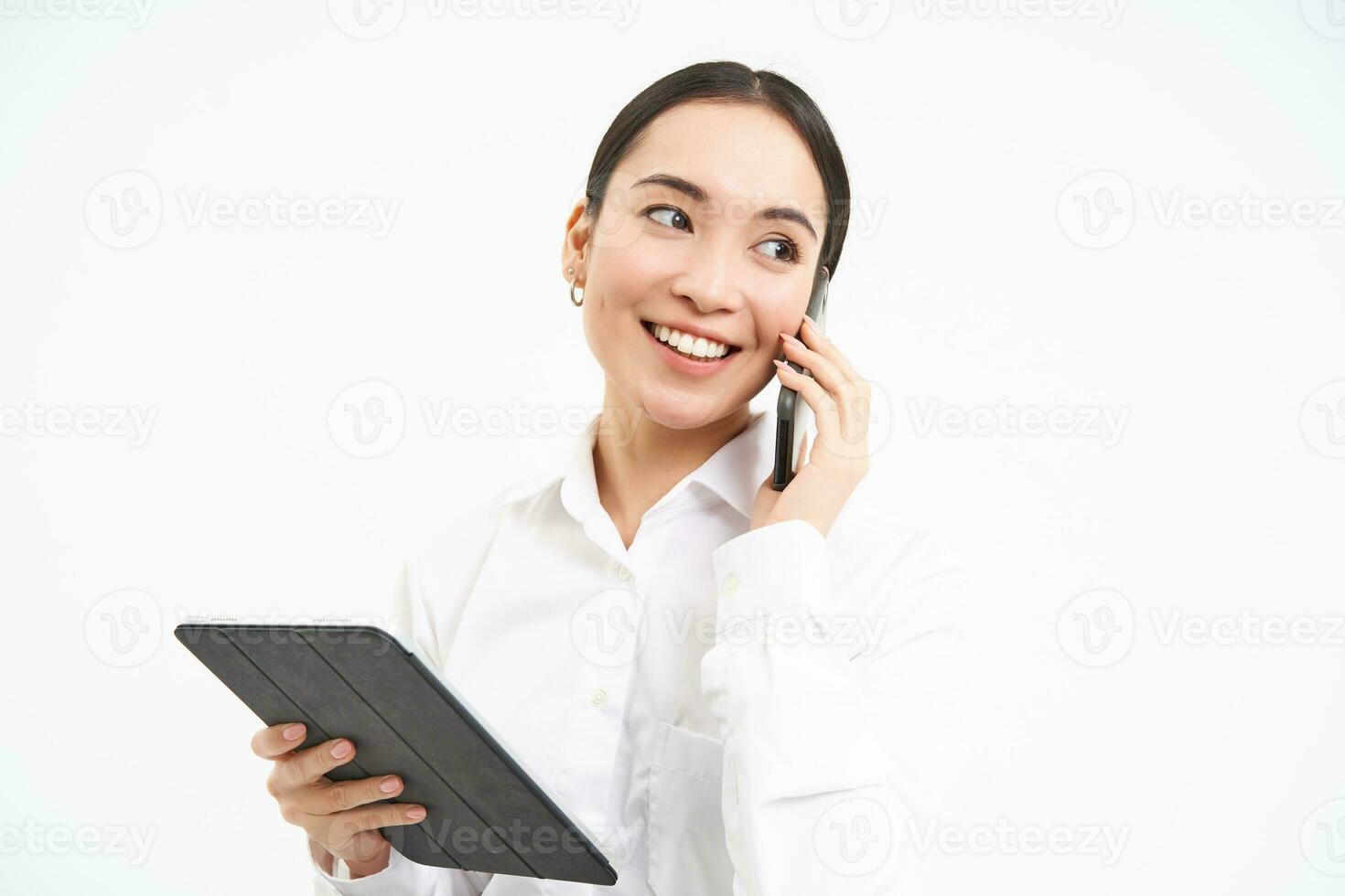 Asian working businesswoman discussing business over the phone, talking on cellphone and looking at digital tablet, standing over white background photo