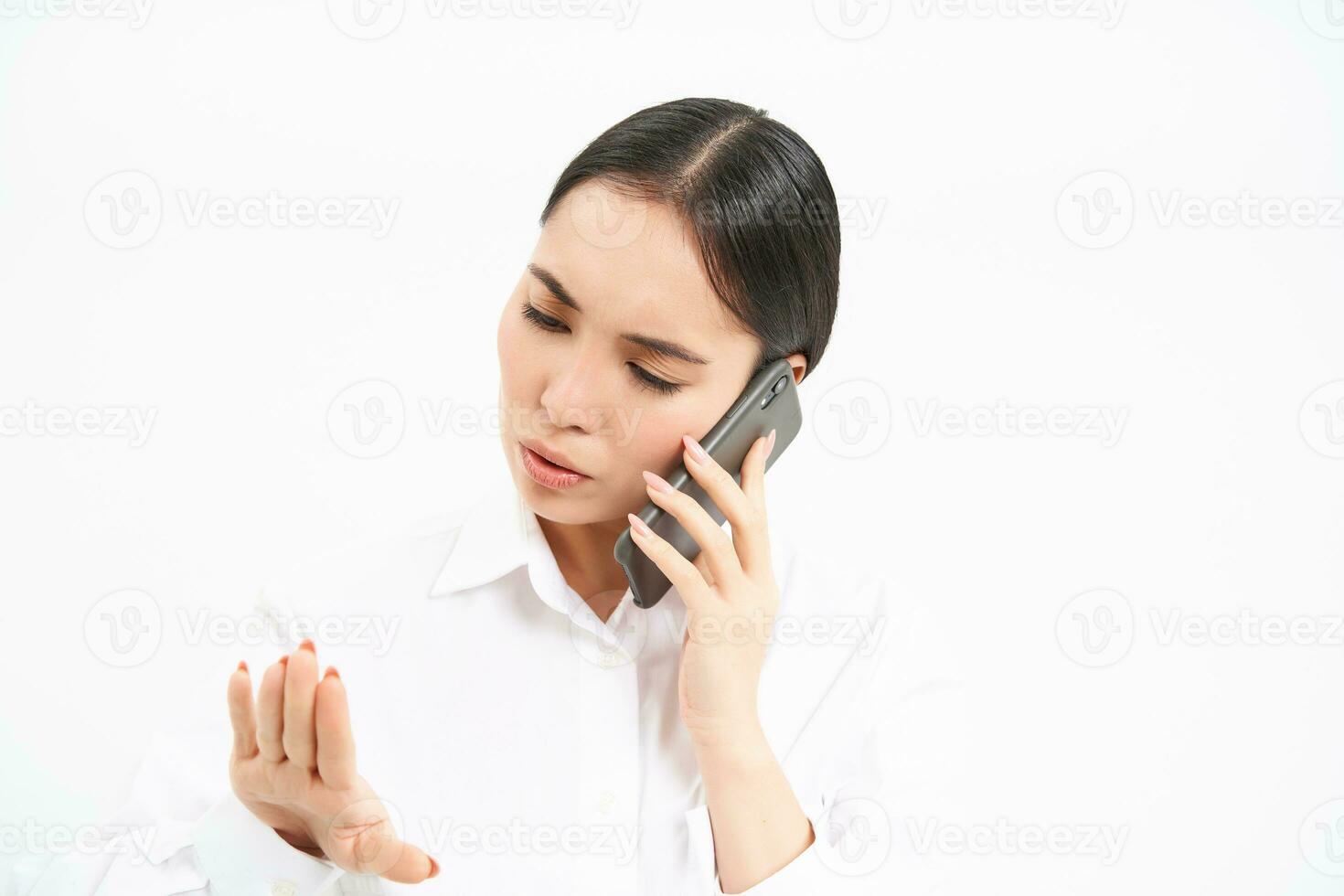 Young corporate employee, woman talks on mobile phone with lack on interest, looks at her nails while listens to person on telephone, white background photo