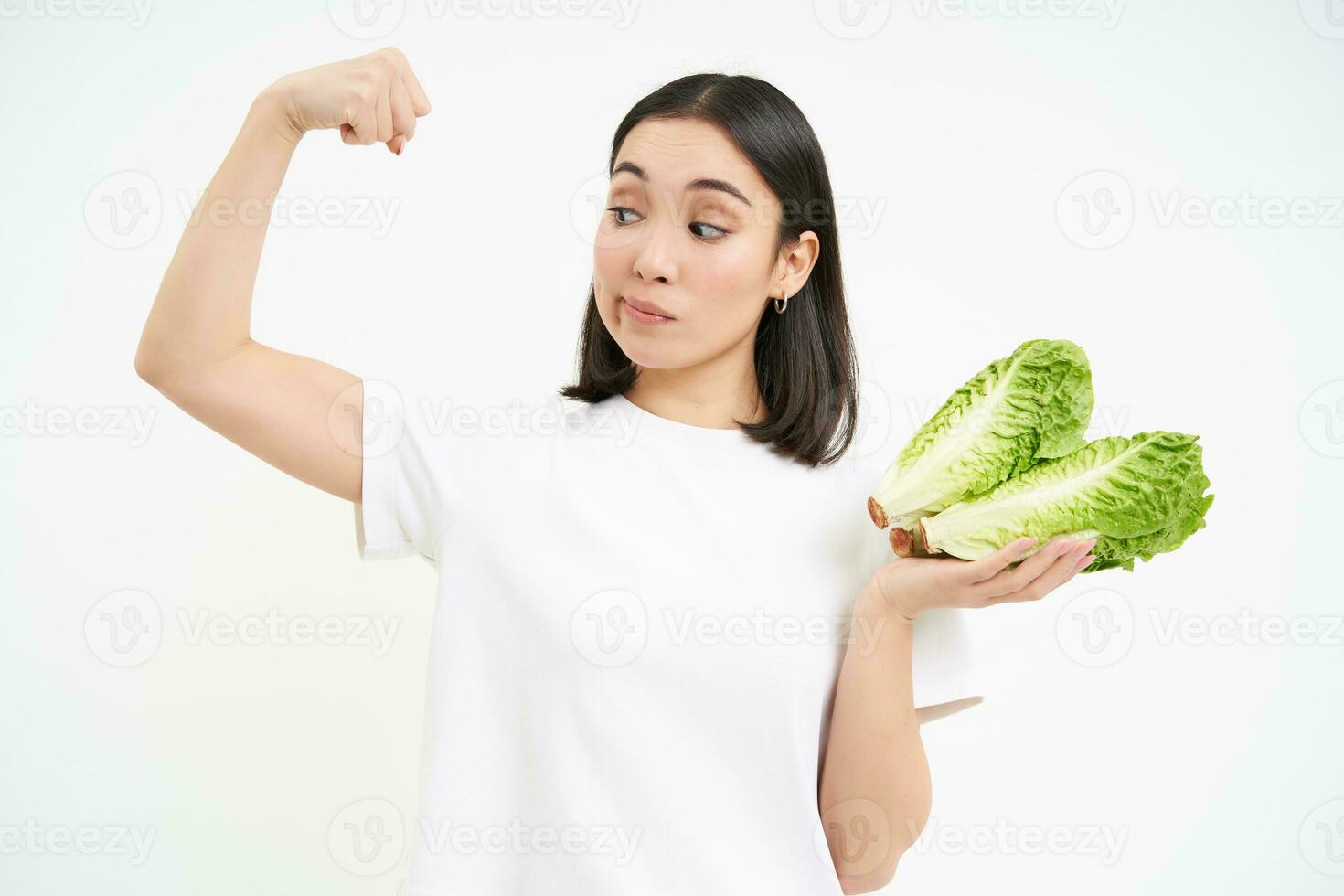 dieta y salud. sonriente asiático mujer muestra su bíceps, fuerte cuerpo y repollo en manos, come vegetales para sano nutrición, blanco antecedentes foto