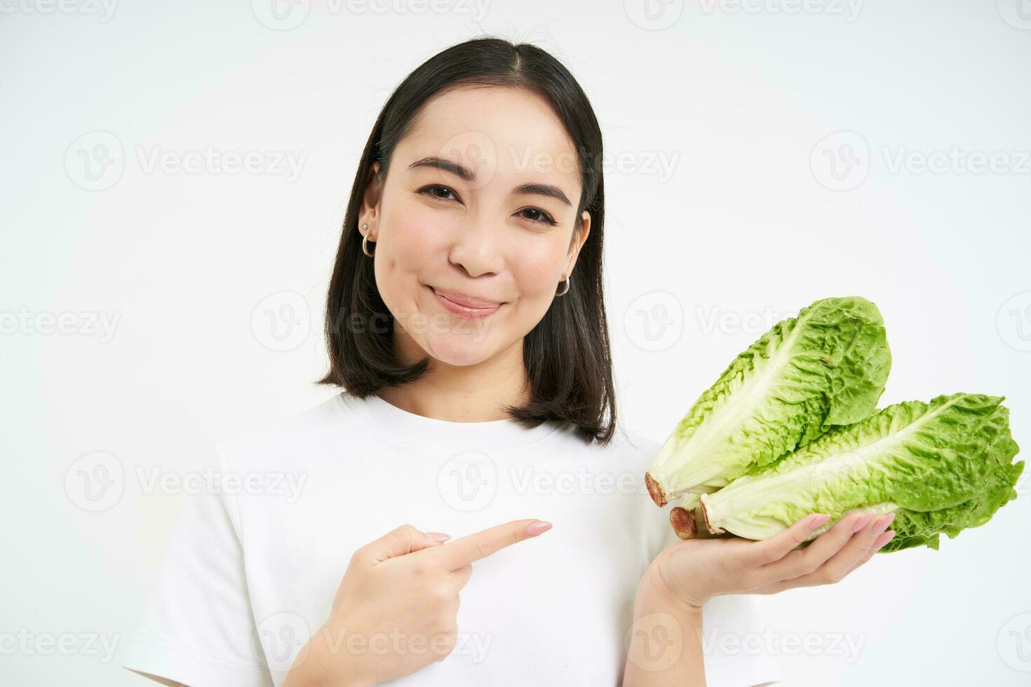 Smiling asian woman, pointing finger at cabbage, grew fresh vegetable, looks happy, isolated on white background photo