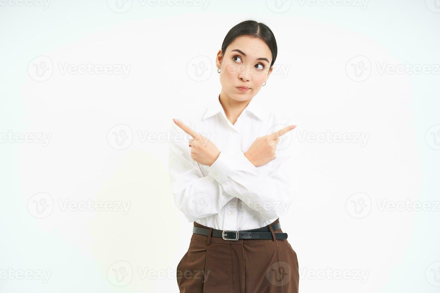 Puzzled businesswoman points sideways, shows two choices, makes decision, stands over white background photo