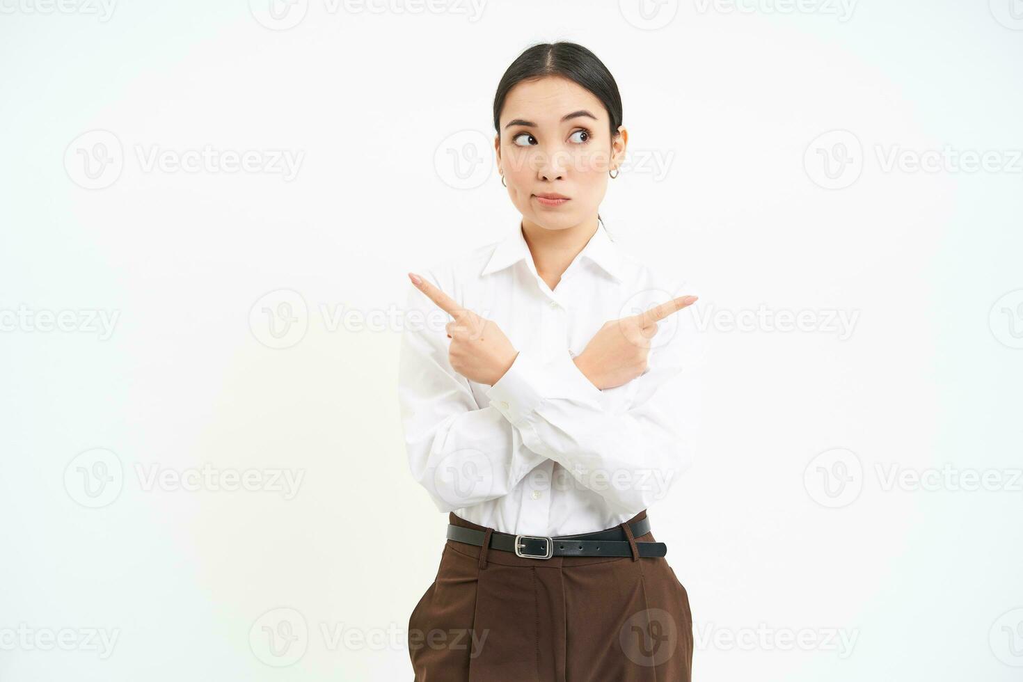 Puzzled businesswoman points sideways, shows two choices, makes decision, stands over white background photo