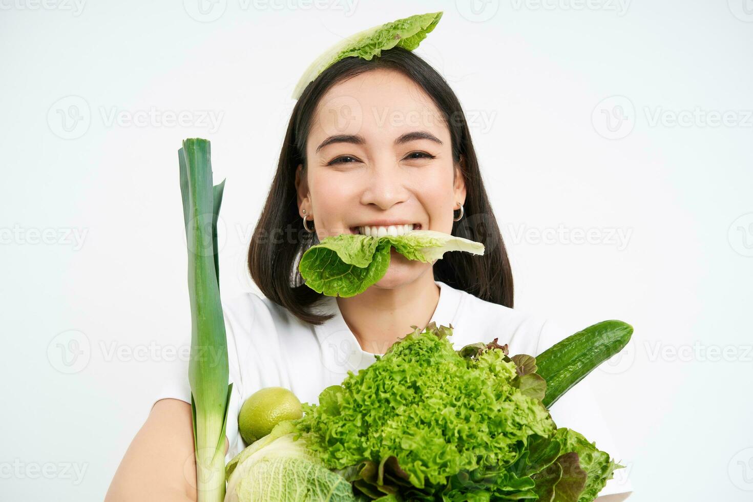 retrato de sonriente coreano mujer come lechuga hoja, participación verde verduras, comiendo nutritivo alimento, blanco antecedentes foto