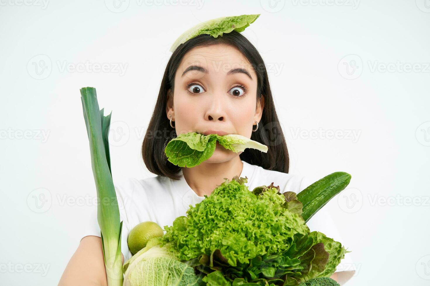 Close up portrait of asian girl munching lettuce leaf, holding green oranic vegetables, leads healthy lifestyle with nutritious food, white background photo