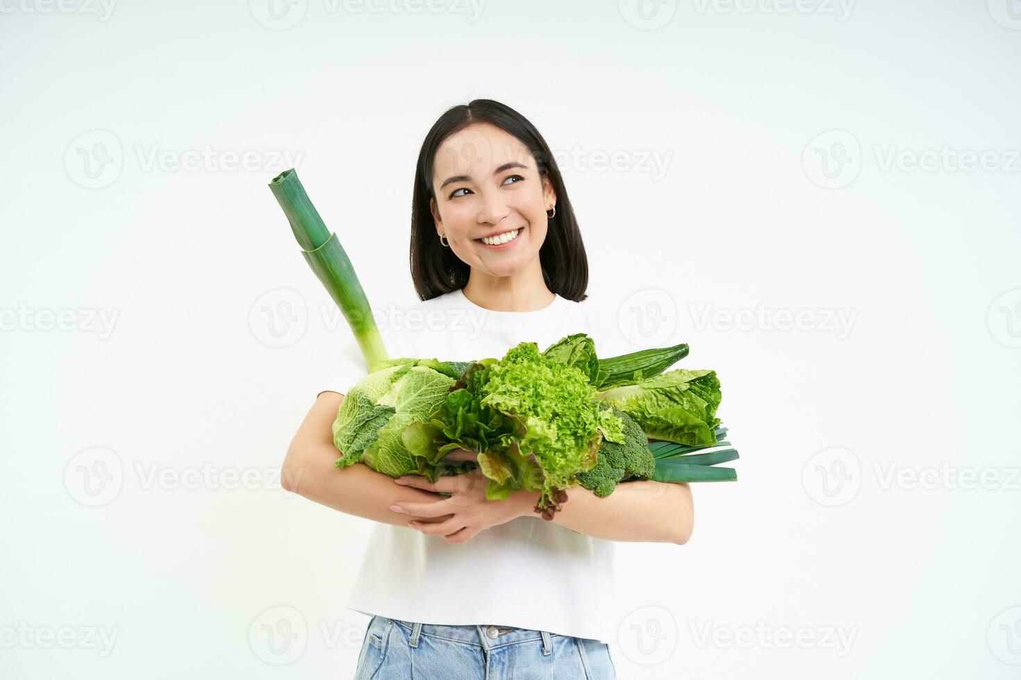 retrato de contento joven mujer en verde dieta, gustos comiendo orgánico alimento, participación Fresco vegetales desde jardín, lechuga, repollo, blanco estudio antecedentes foto