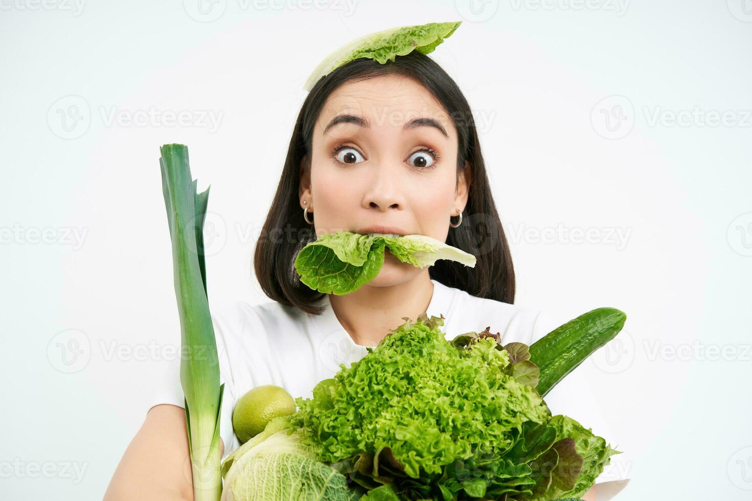 Close up portrait of asian girl munching lettuce leaf, holding green oranic vegetables, leads healthy lifestyle with nutritious food, white background photo