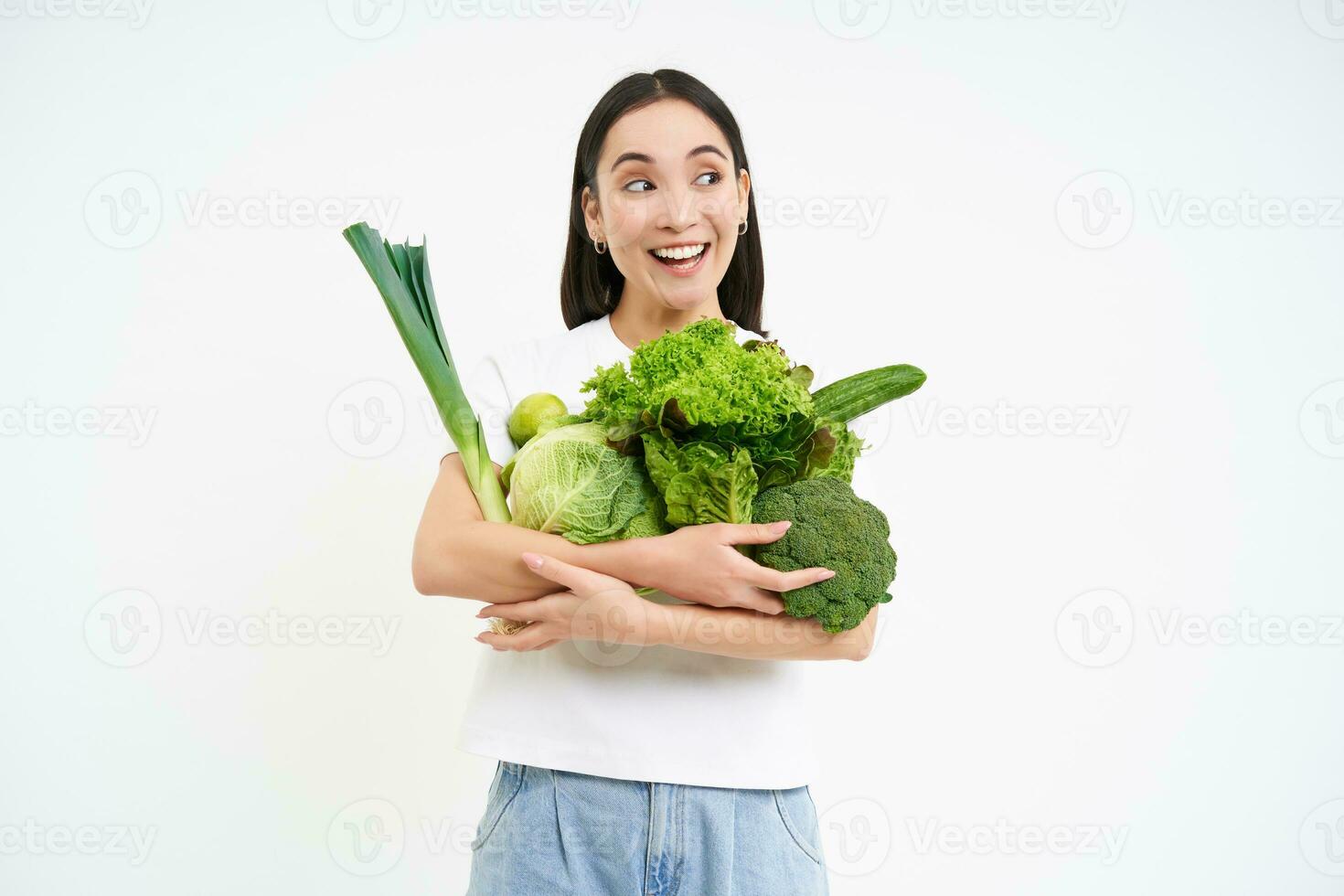 retrato de sonriente coreano mujer, abrazos su verduras, gustos comiendo crudo alimento, vegetariano disfruta nutritivo dieta, blanco antecedentes foto