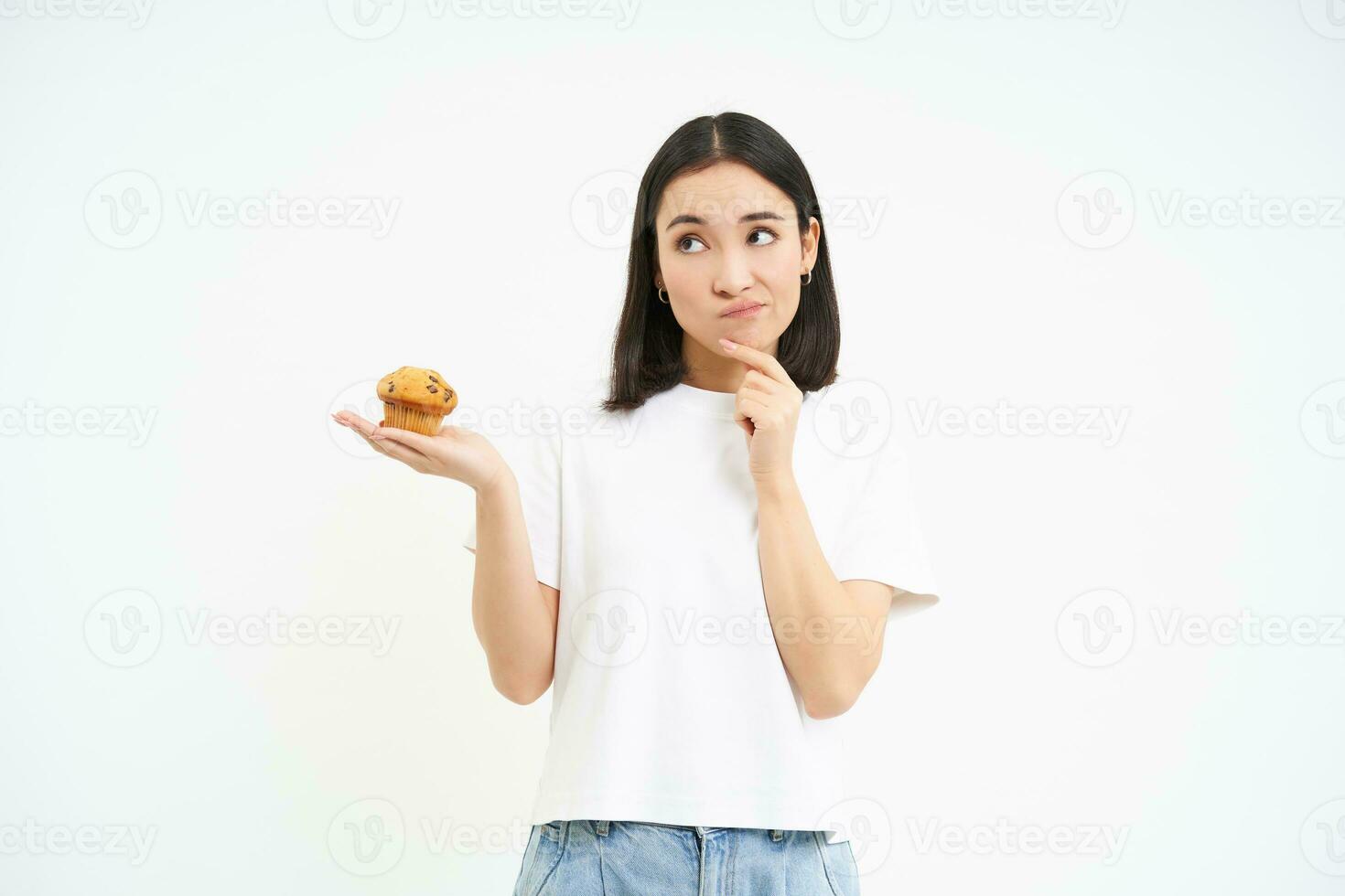 Woman with pensive face, holding cupcake and thinking, white background photo