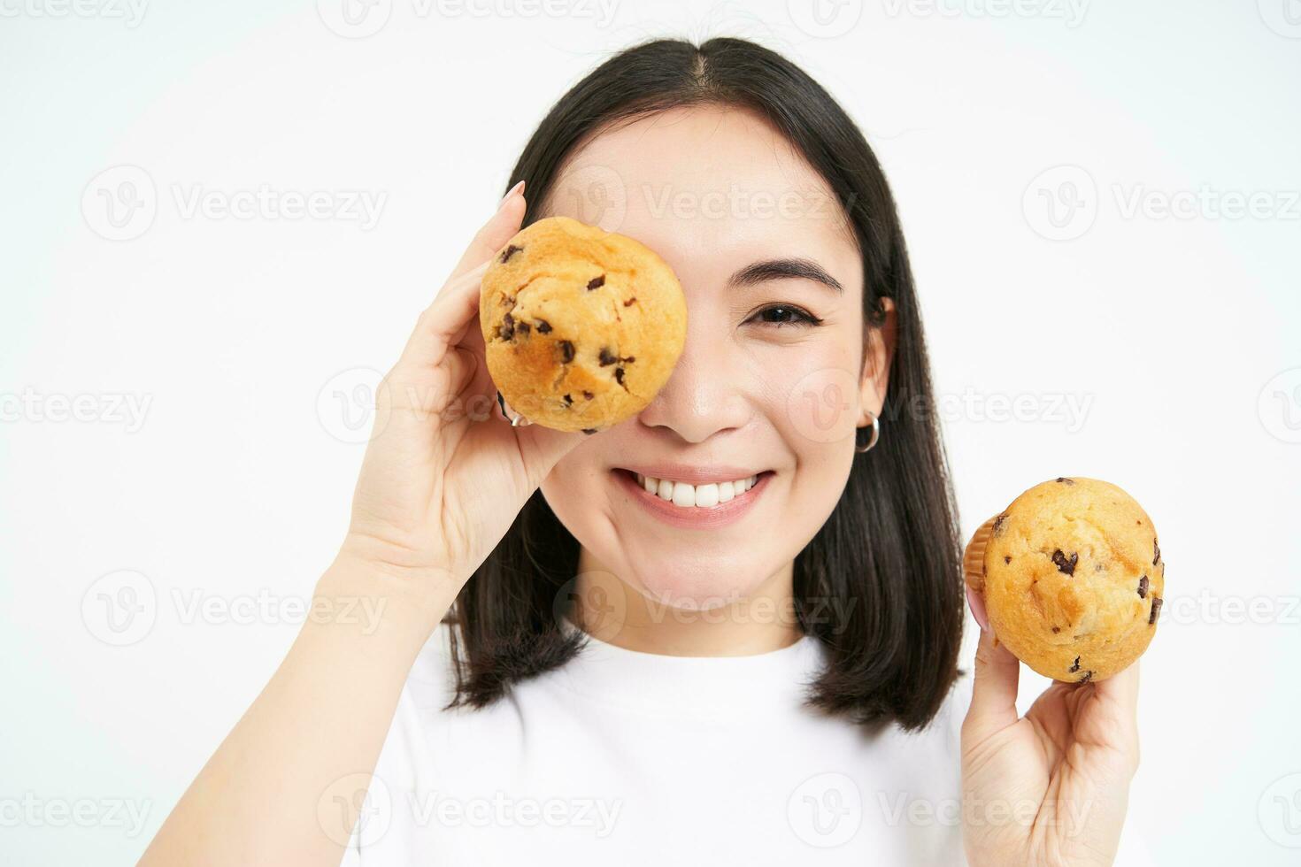 Close up portrait of smiling korean woman, shows tasty cupcakes, eating cake and looking happy, pastry and bakery concept photo