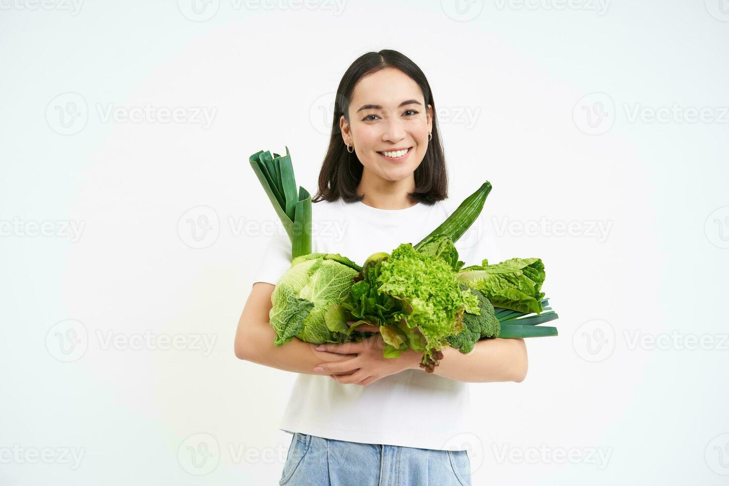 Image of smiling asian woman, vegetarian with lots of green vegetables, eating oranic food, isolated on white background photo