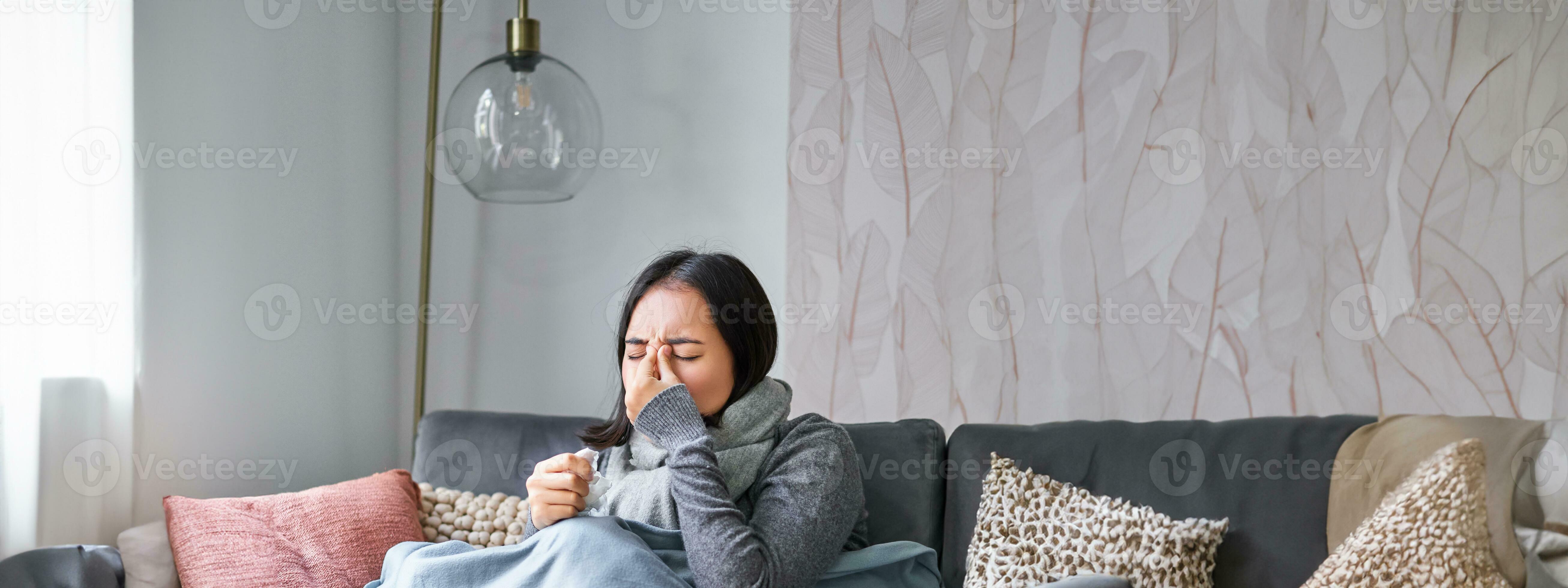 Woman with temperature, coughing, showing symptoms of flu, influenza or cold, sitting in warm