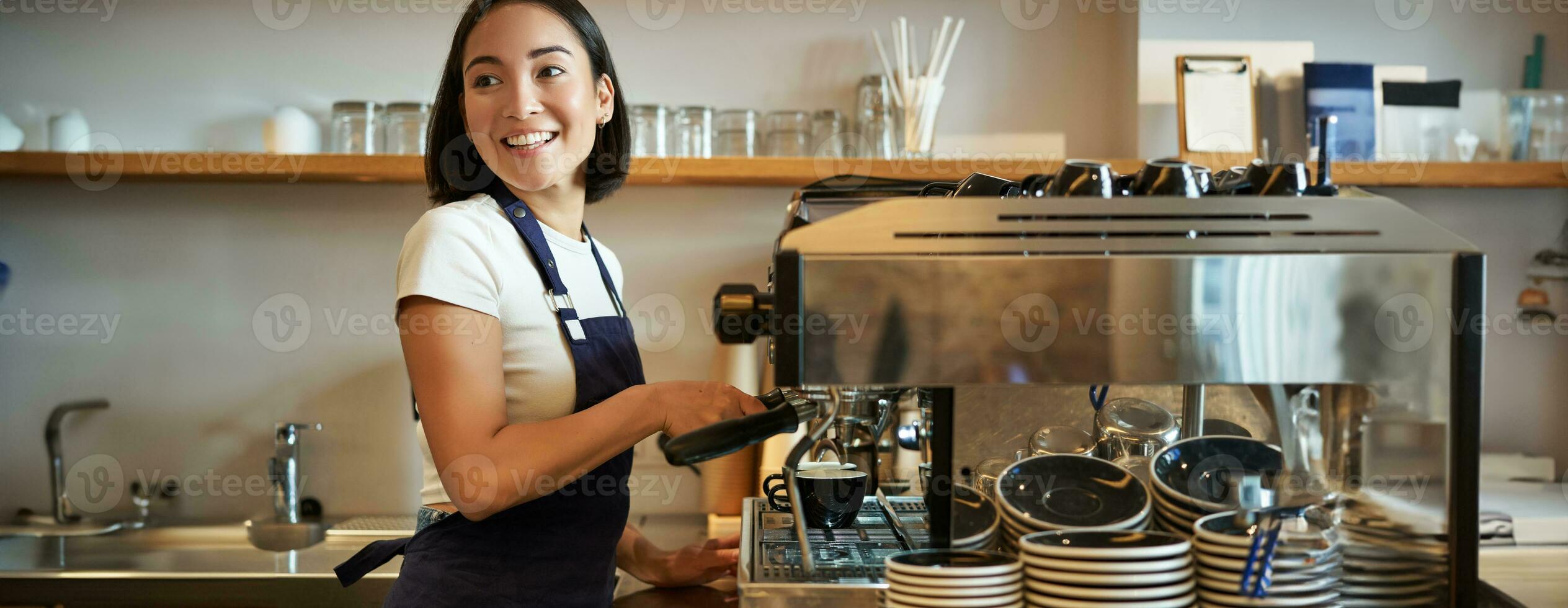 Happy smiling bartender, barista using coffee machine, prepare order, making cappuccino or latte, wearing blue apron photo