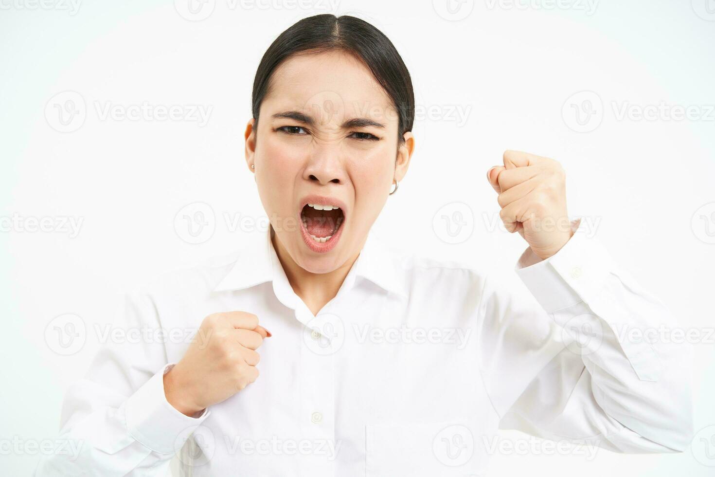 Angry asian woman yells and shakes fists, shouts at employees, stands frustrated against white background photo