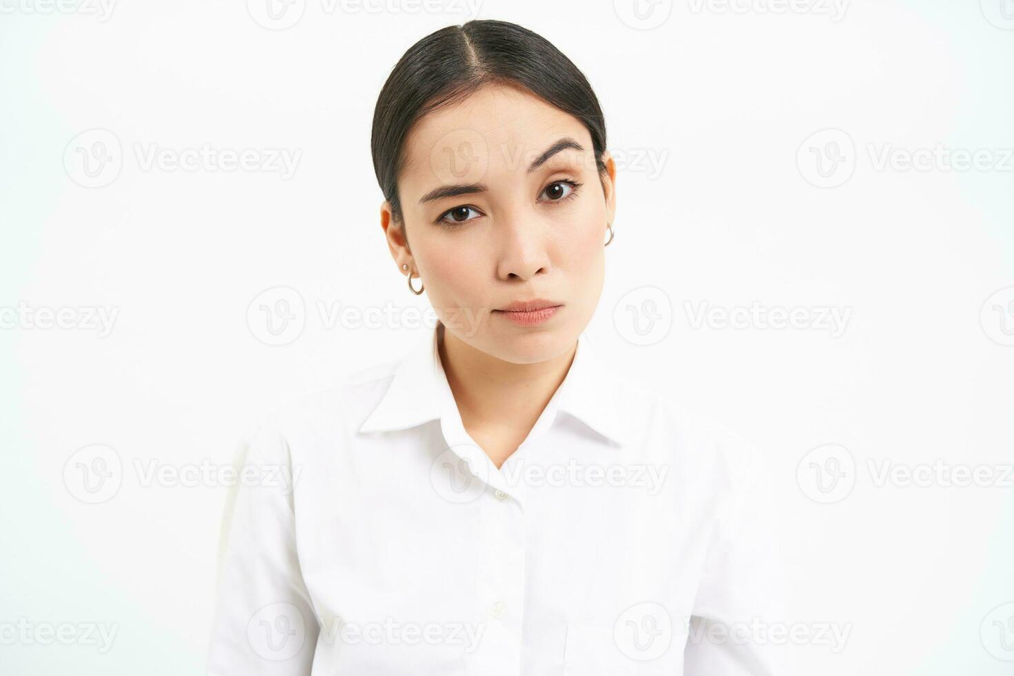 Portrait of skeptical asian woman, looks unamused and serious at camera, stands isolated on white background photo