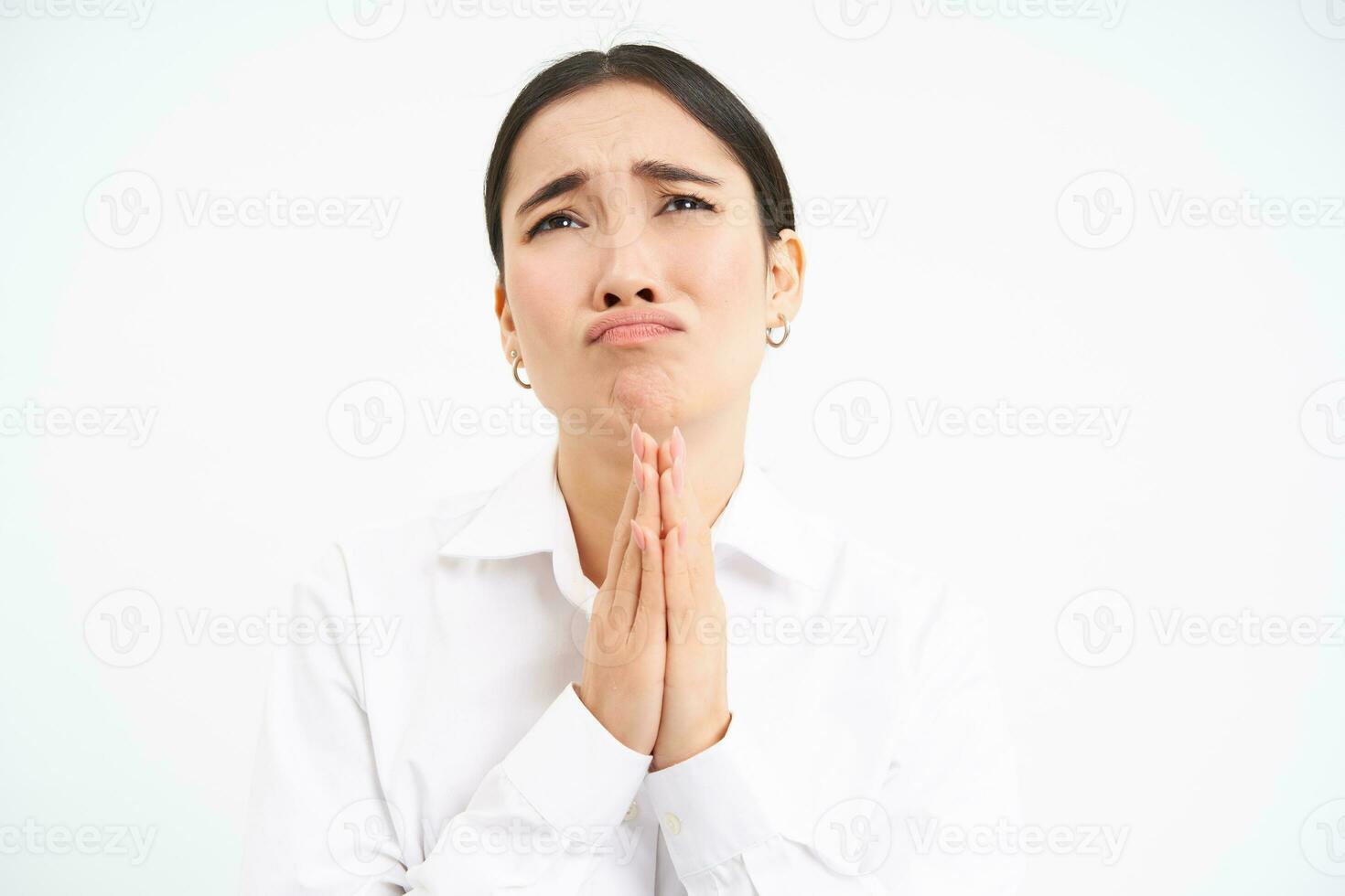 Upset asian woman looks up with desperate and sad face, complains to Lord, stands over white background photo