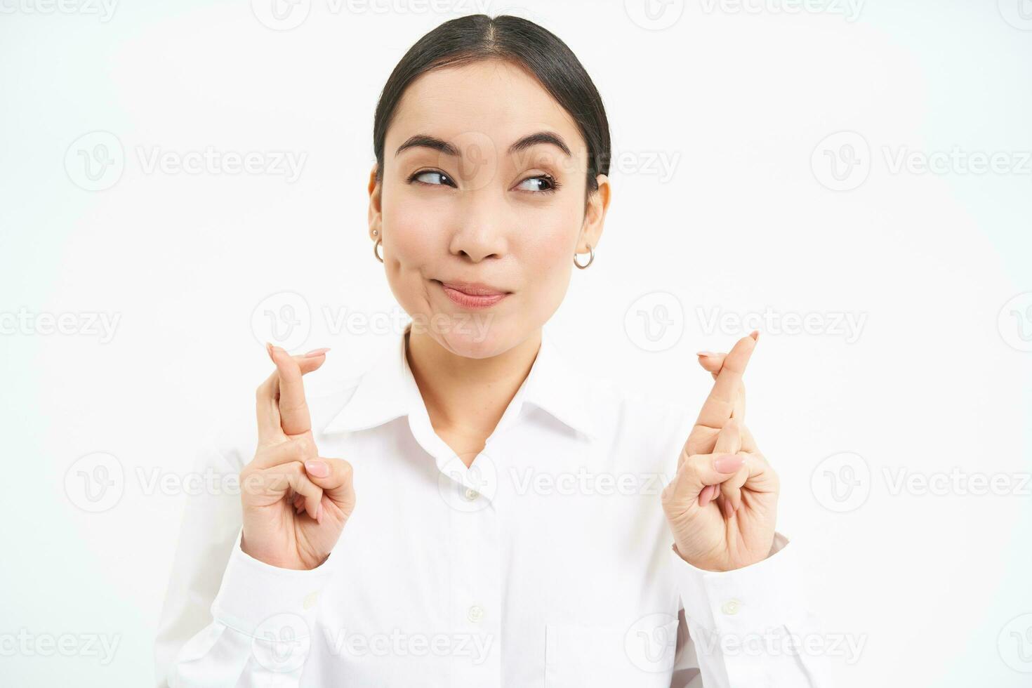 Close up portrait of hopeful businesswoman, cross fingers for good luck, waits for something, makes wish, smiles and anticipates, white studio background photo