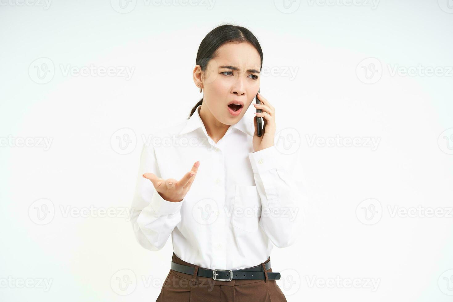 Angry business woman shouts at mobile phone, has intense conversation on telephone, stands over white background photo