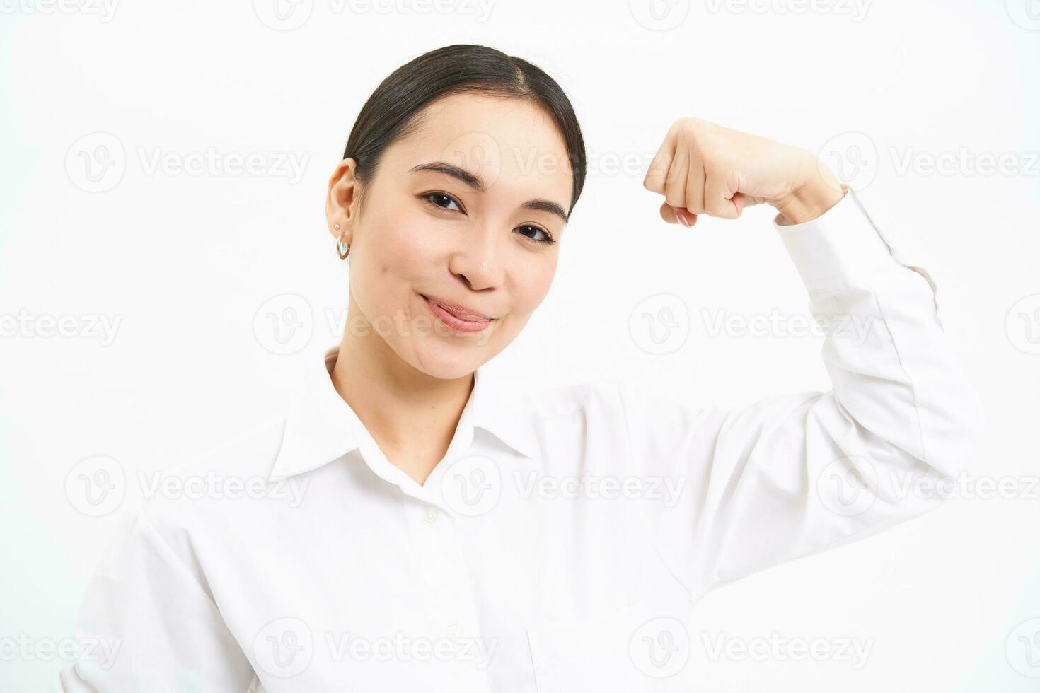 Portrait of confident and strong businesswoman, flexing biceps, shows strength, muscles, stands over white background photo