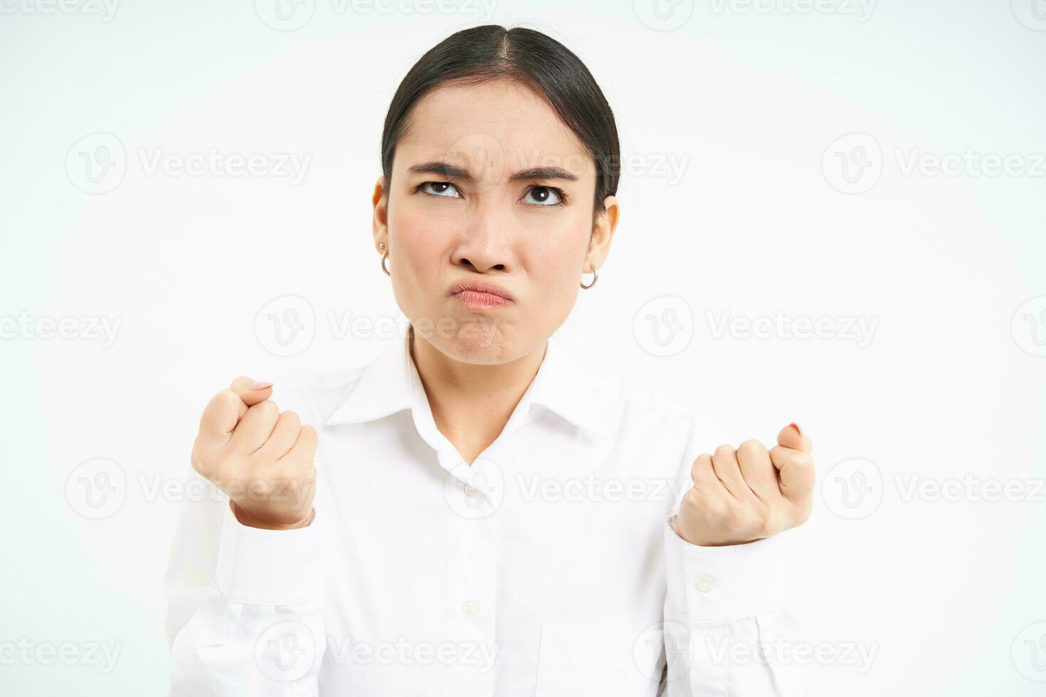 Portrait of angry, pissed-off businesswoman, japanese lady clenches fists and looks up with bothered, frustrated face expression, standing over white background photo