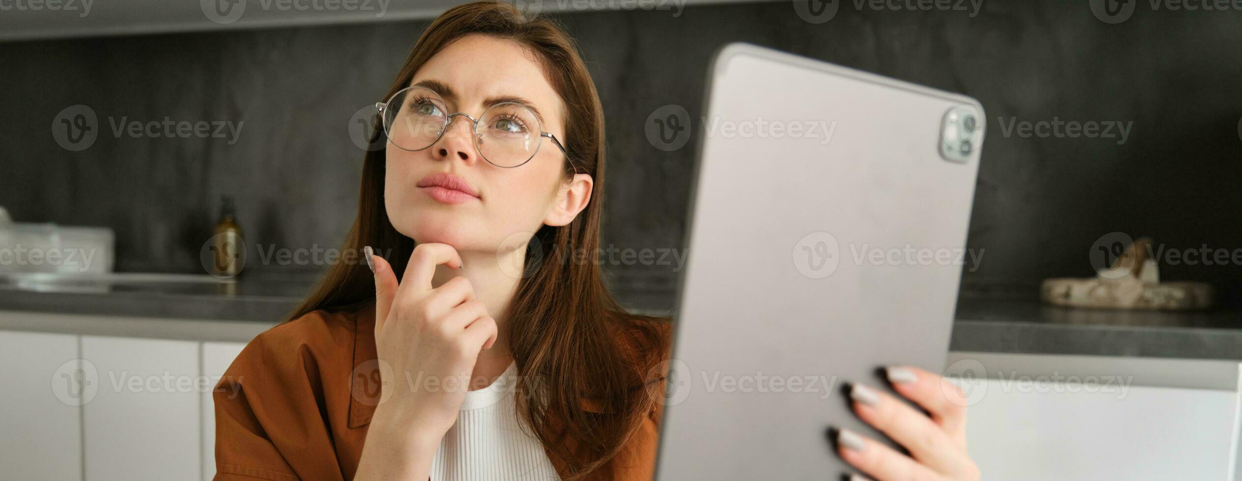 Close up portrait of serious woman working from home, holding digital tablet, looking aside with thinking face, pondering, studying online, works on remote photo