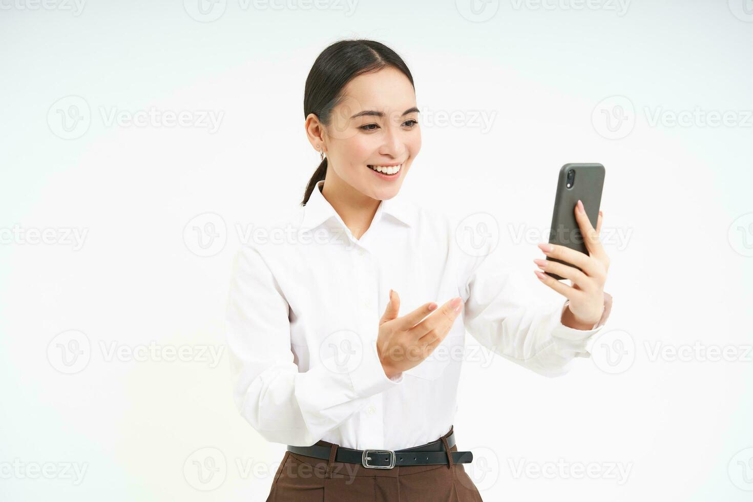 Portrait of corporate woman, manager video chats on mobile phone, looks at smartphone and leads a meeting online via smartphone app, white background photo