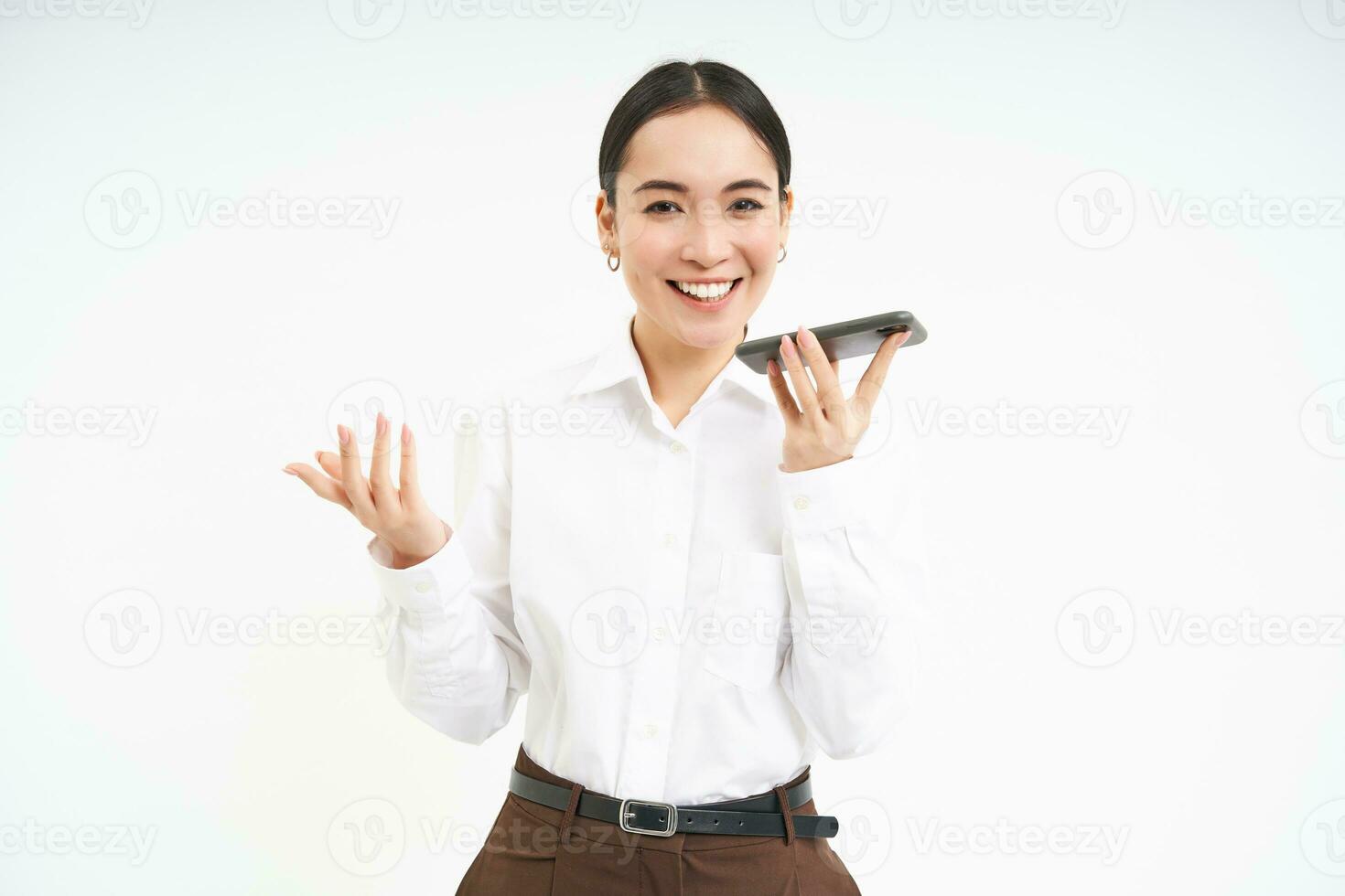 sonriente hembra vendedora, asiático mujer gerente negociaciones en altavoz teléfono, sostiene Teléfono móvil cerca boca y traduce su discurso, blanco antecedentes foto
