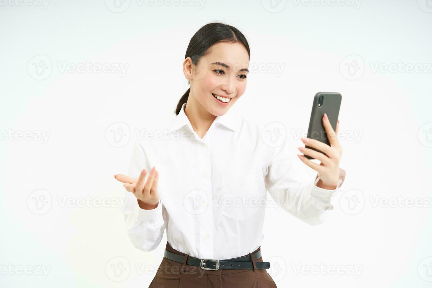 Portrait of corporate woman, manager video chats on mobile phone, looks at smartphone and leads a meeting online via smartphone app, white background photo