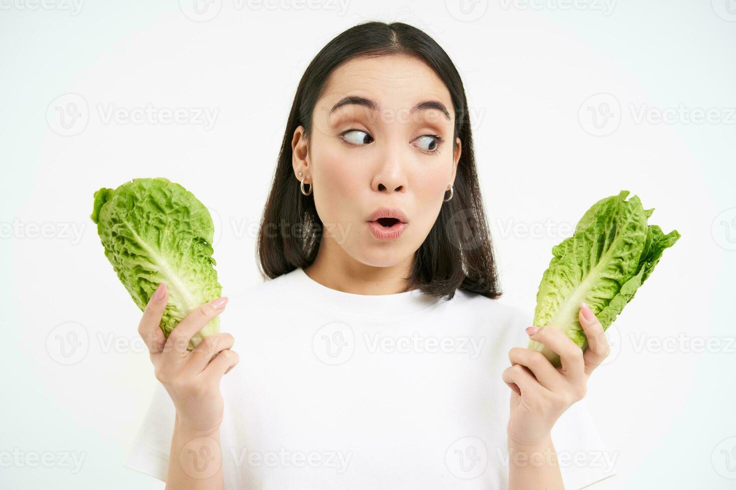 Portrait of woman with surprised face, holding cabbage, lettuce leaves and looks amazed, growing vegetables in own garden, white background photo
