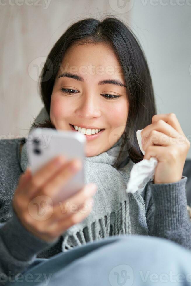 Portrait of korean woman feels sick, holding smartphone, calling doctor gp to get presctiption, caught cold, staying at home, using mobile phone photo