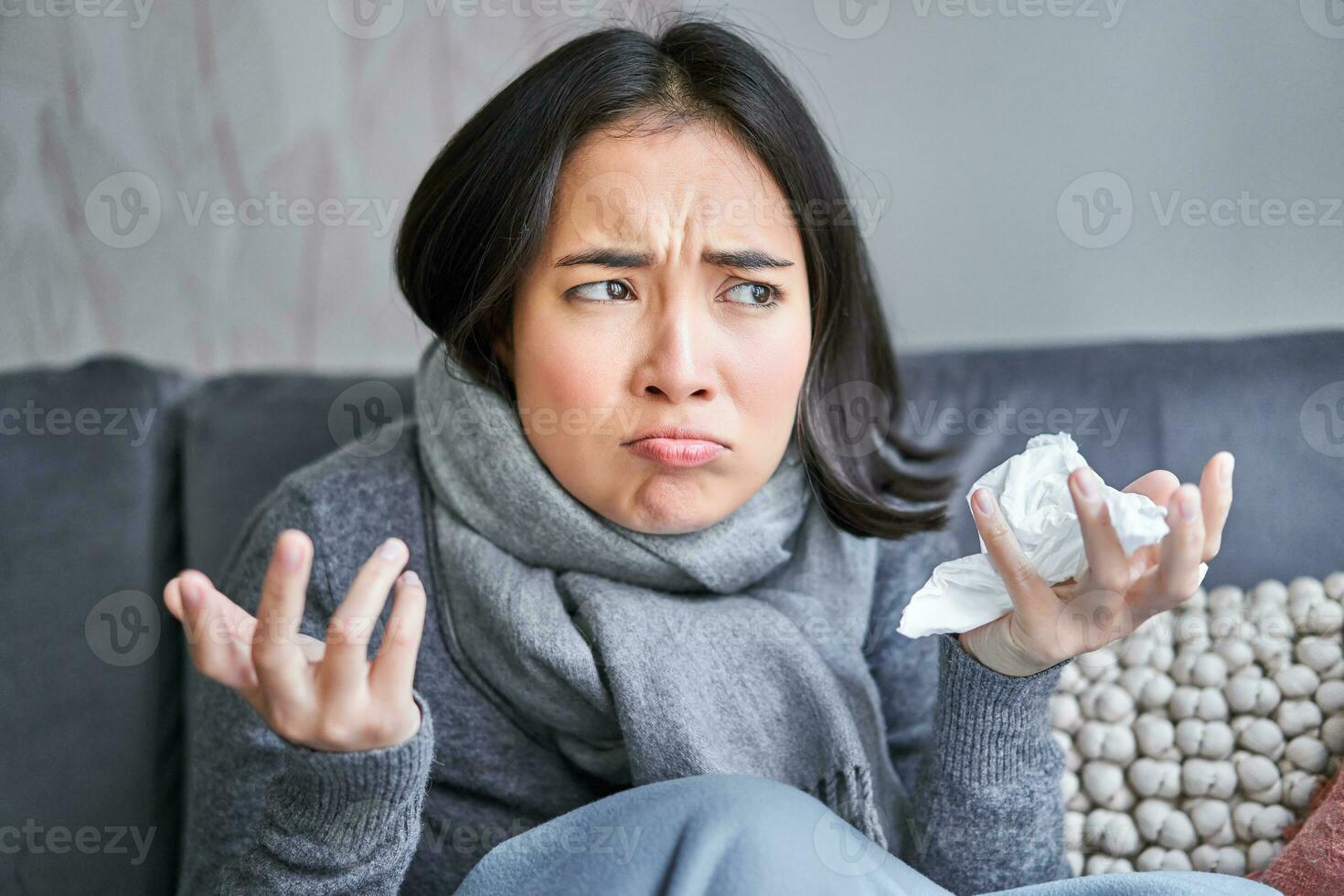 Cost of living and heating problems. Close up of angry girl sneezing, staying at home and freezing, wearing warm clothes and scarf photo