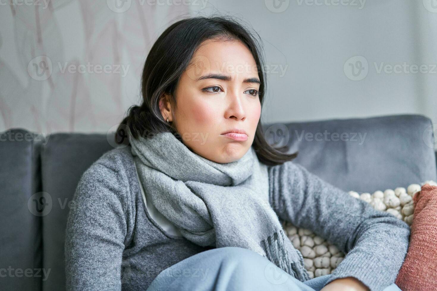 Portrait of sad woman feeling unwell, wearing warm clothes and scarf at her home without heating, staying on sick leave in her house photo